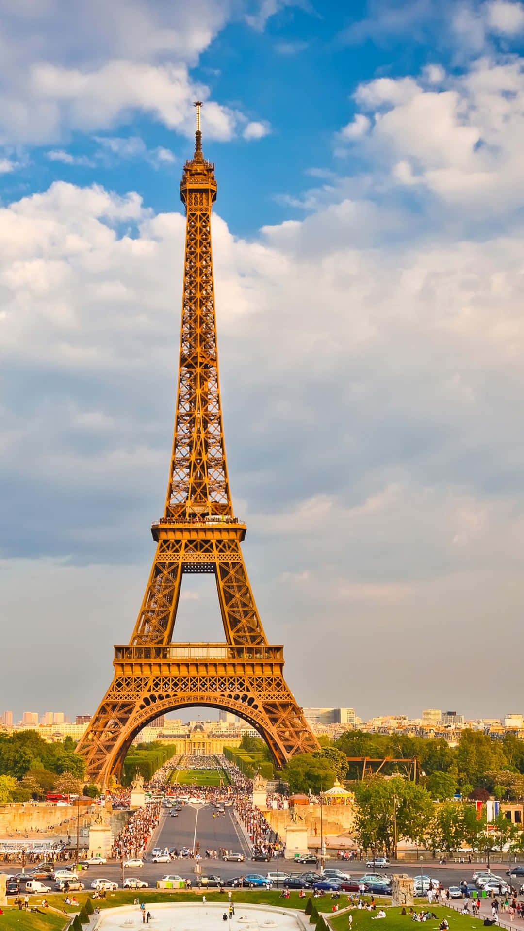 Eiffel Tower 桌布 壁紙 — 艾菲爾鐵塔高聳入雲，天空部分多雲，金色陽光灑在其鐵結構和下方熙攘的戰神廣場上。