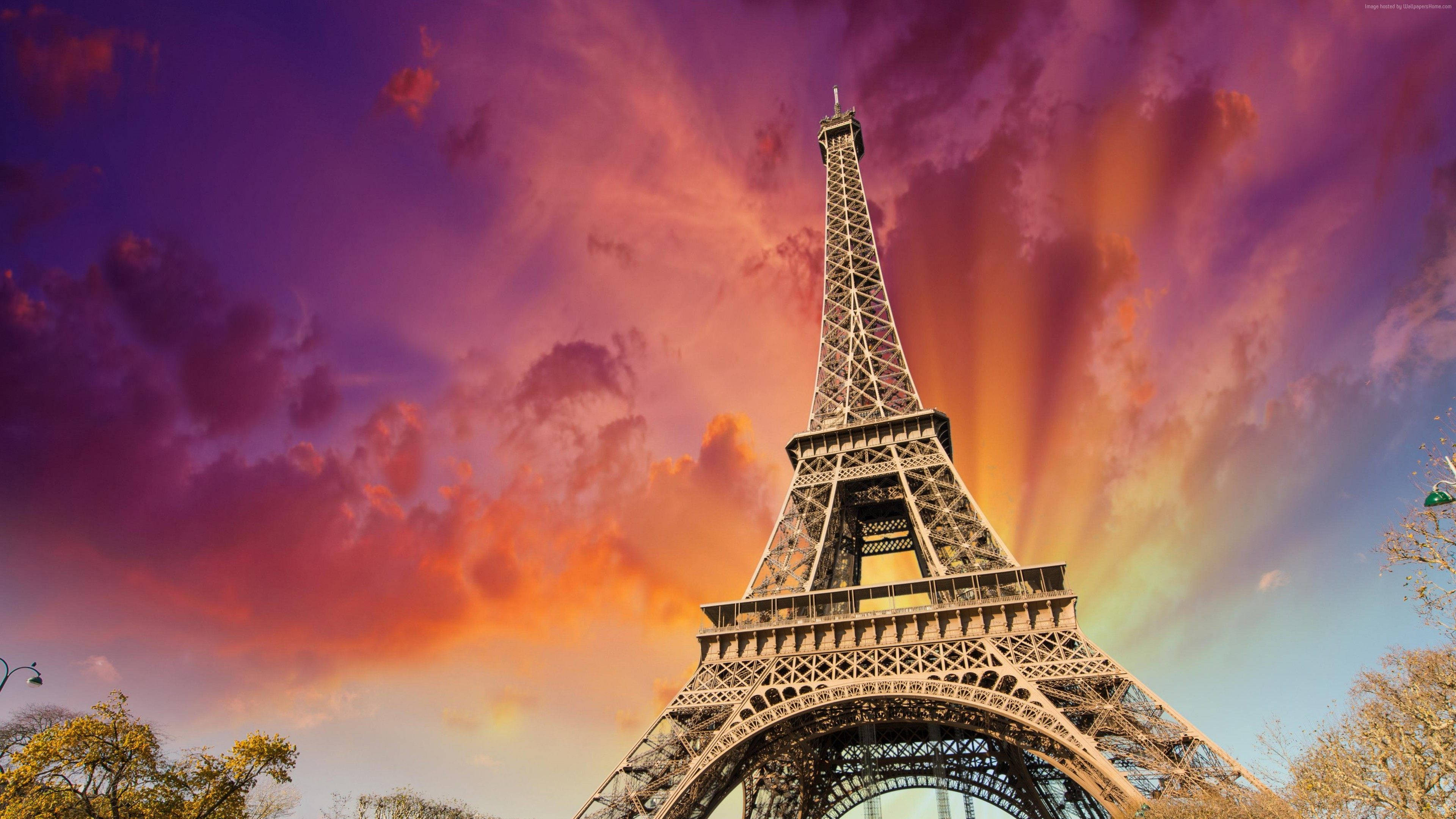Eiffel Tower 桌布 壁紙 — 艾菲爾鐵塔高聳入雲，映襯著由火橙色和深紫色雲彩繪成的戲劇性日落天空。