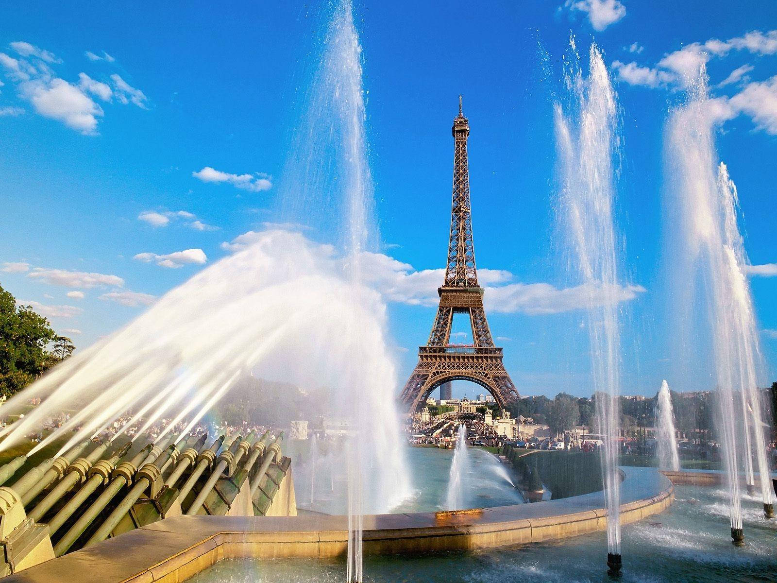 Paris Eiffel Tower 桌布 壁紙 — 艾菲爾鐵塔高聳在活潑的噴泉後面，噴泉在明亮的藍天和白雲下噴水。