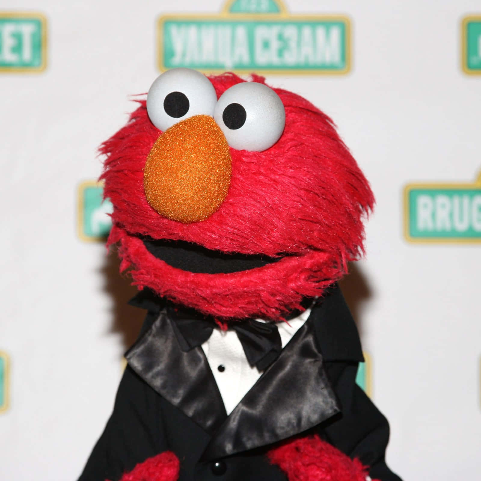 Elmo 桌布 壁紙 — 艾蒙穿著黑色燕尾服和領結，在品牌背景前的特寫。