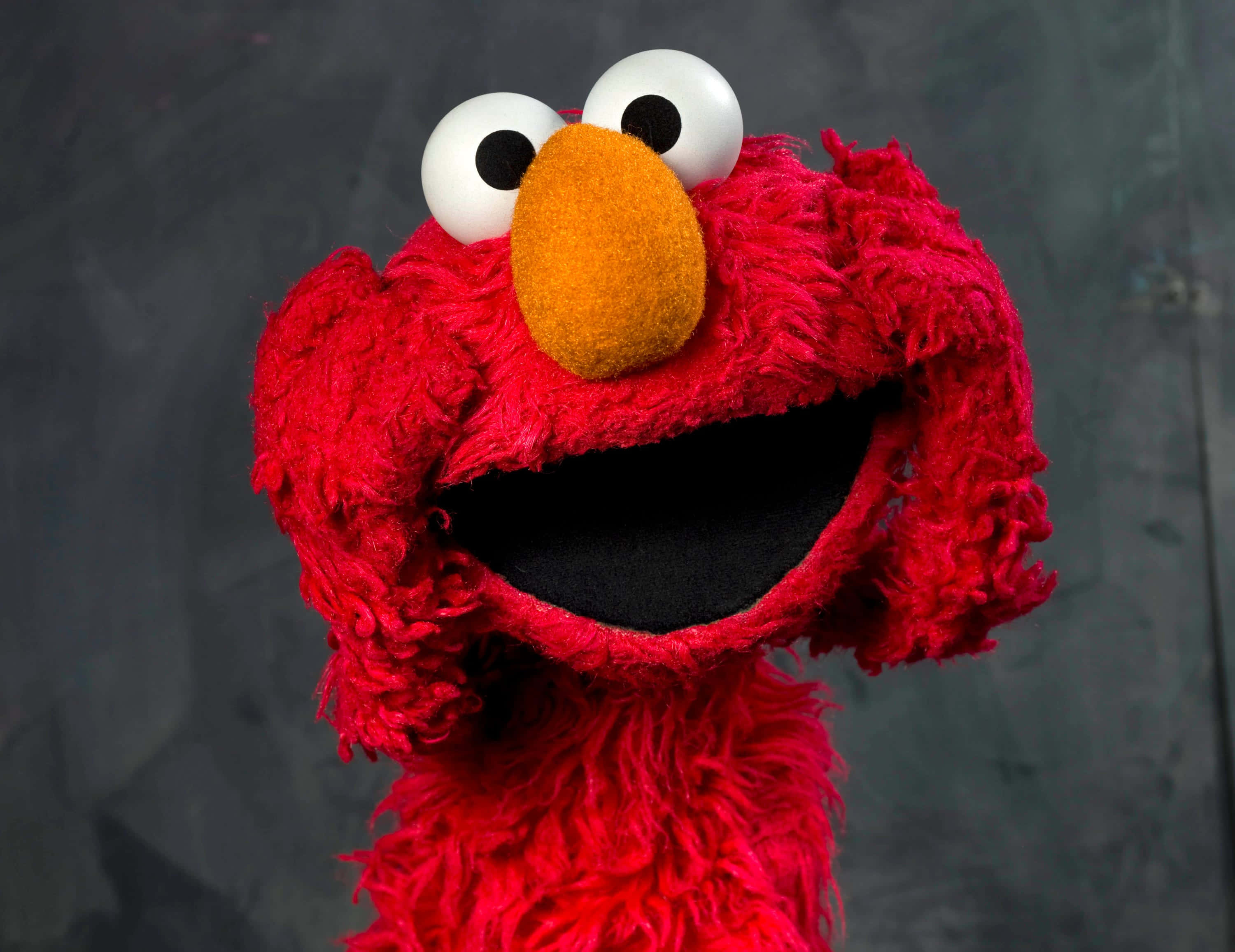 Sesame Street 桌布 壁紙 — 艾蒙開心紅色毛茸茸臉部的特寫，有大大的白色眼睛和橙色鼻子，背景為深灰色。