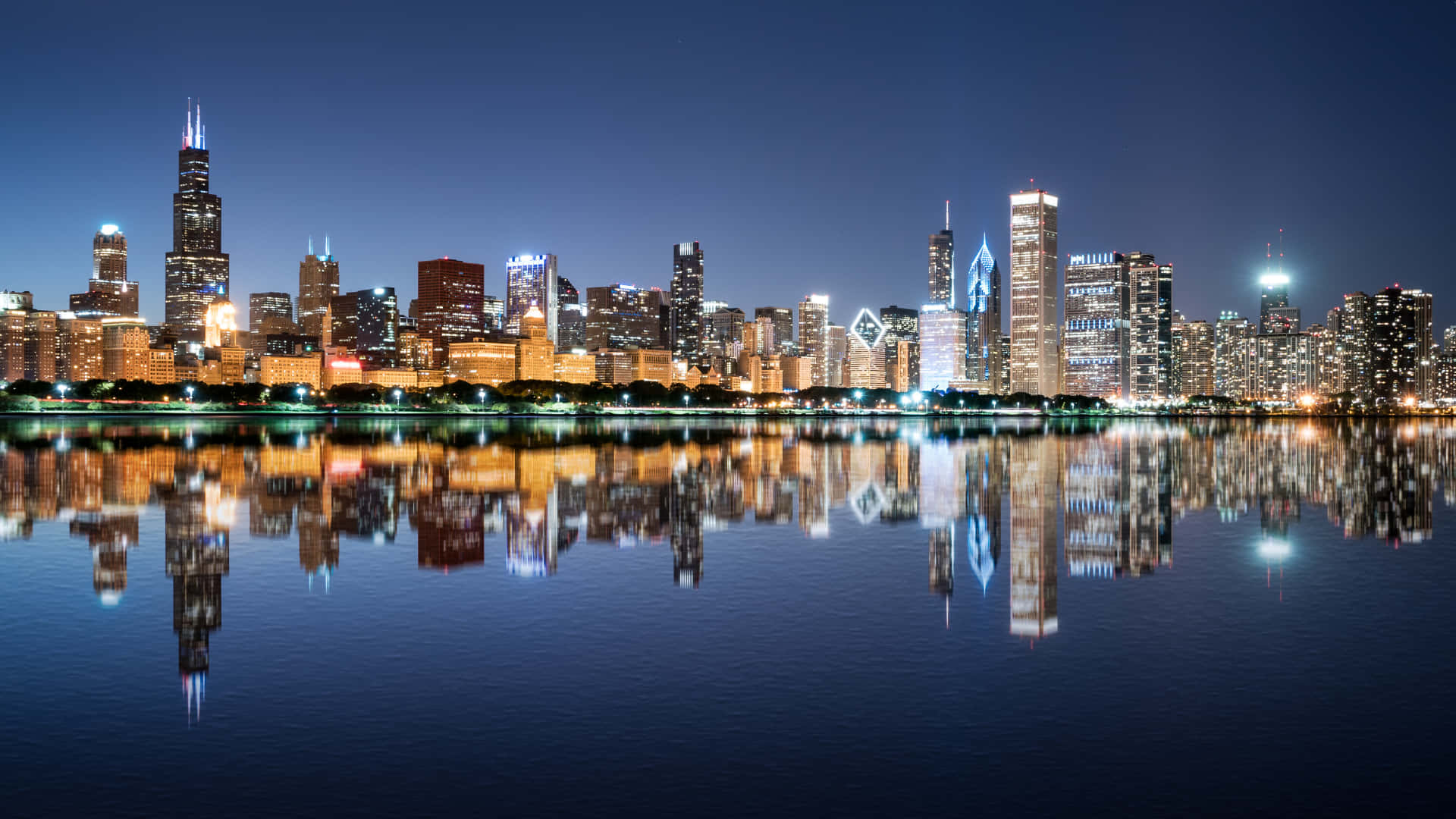 City View 桌布 壁紙 — 芝加哥天際線夜景，燈火通明的摩天大樓在深藍色天空下平靜的水面上完美倒映。
