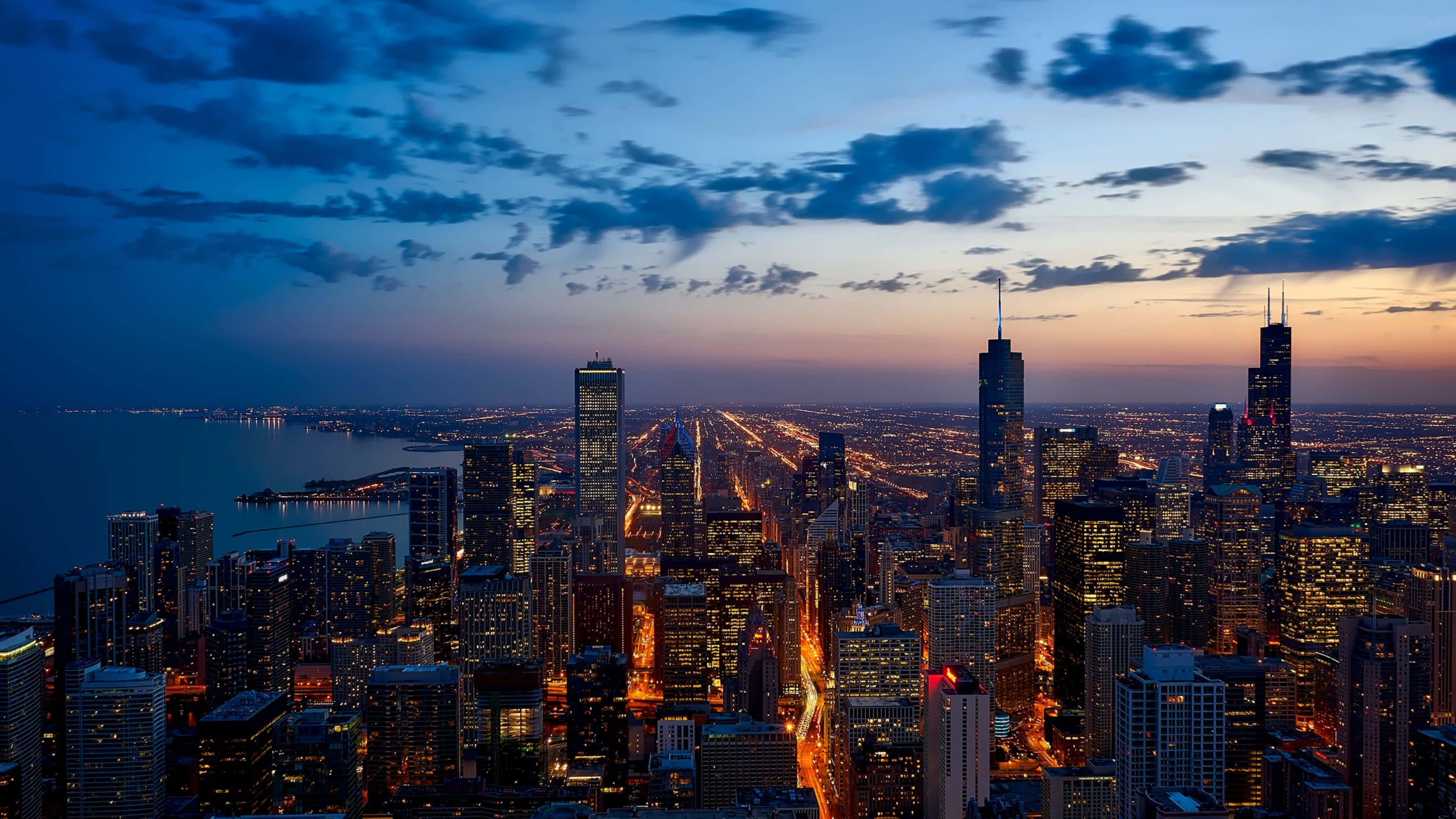 4K Ultra HD Chicago 桌布 壁紙 — 芝加哥天際線的鳥瞰圖，在黃昏時分，摩天大樓閃閃發光，密西根湖上空呈現充滿活力的橙色地平線。