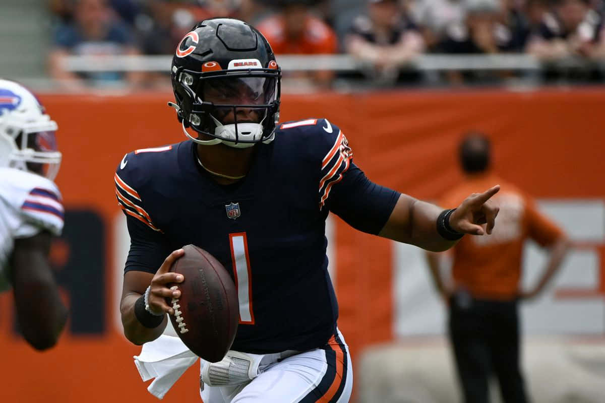Justin Fields 桌布 壁紙 — 芝加哥熊隊四分衛身穿海軍藍球衣，背號1號，在NFL比賽中擲出橄欖球，背景為模糊的體育場。