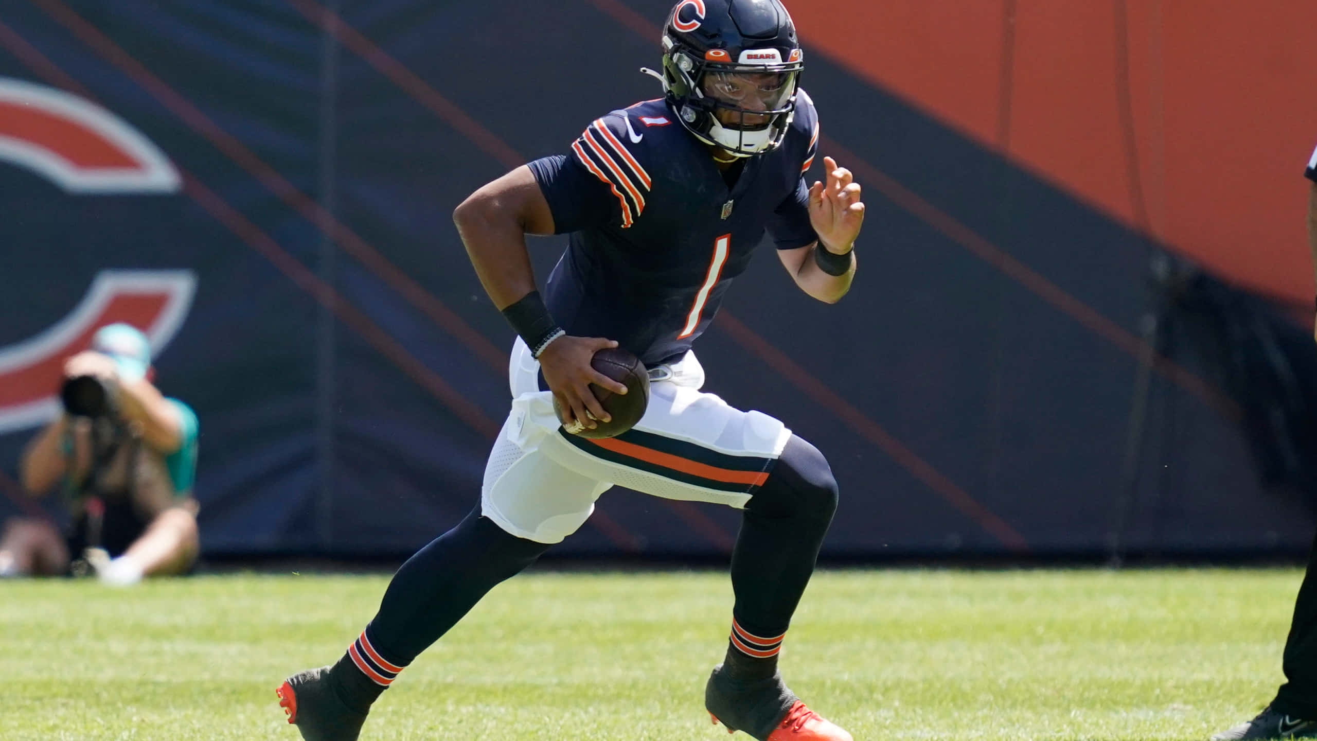Justin Fields 桌布 壁紙 — 芝加哥熊隊四分衛身穿海軍藍球衣和白色長褲，在陽光明媚的草地上準備擲出橄欖球。