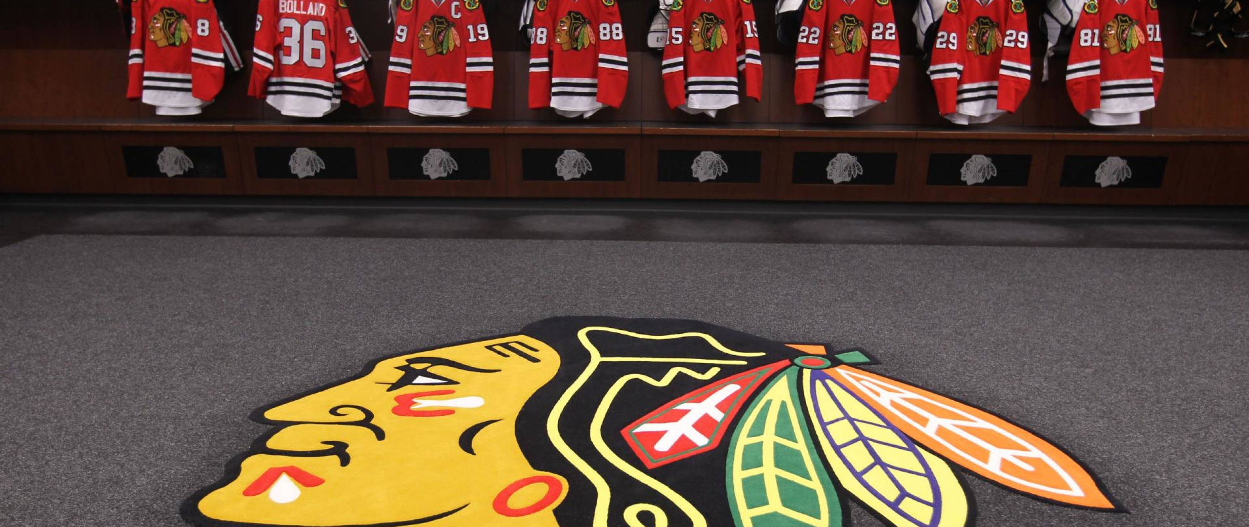 Blackhawks 桌布 壁紙 — 芝加哥黑鷹隊標誌地毯在更衣室，紅色球衣掛在木長凳上。
