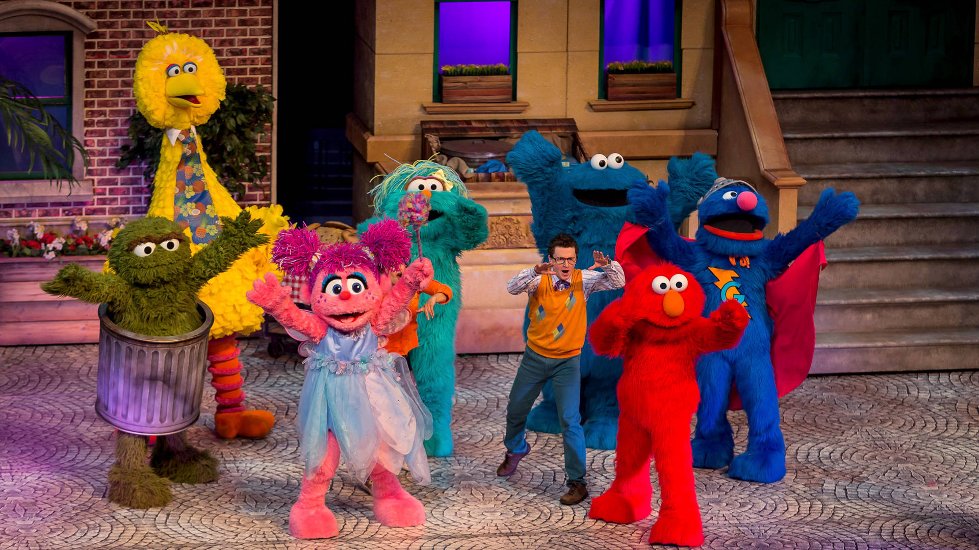 芝麻街 桌布 壁紙 — 芝麻街角色，包括 Elmo、Big Bird 和 Cookie Monster，在建築物前的磚砌人行道上愉快地擺姿勢。