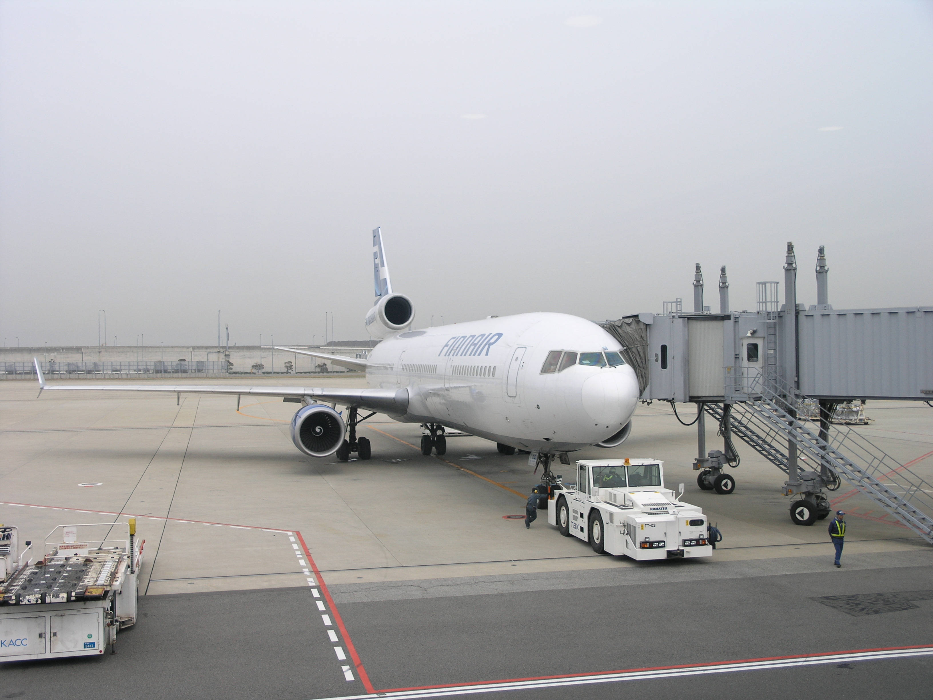 Airport 桌布 壁紙 — 芬蘭航空飛機停泊在機場閘口，連接了登機橋，地勤人員在附近，天色陰沉。