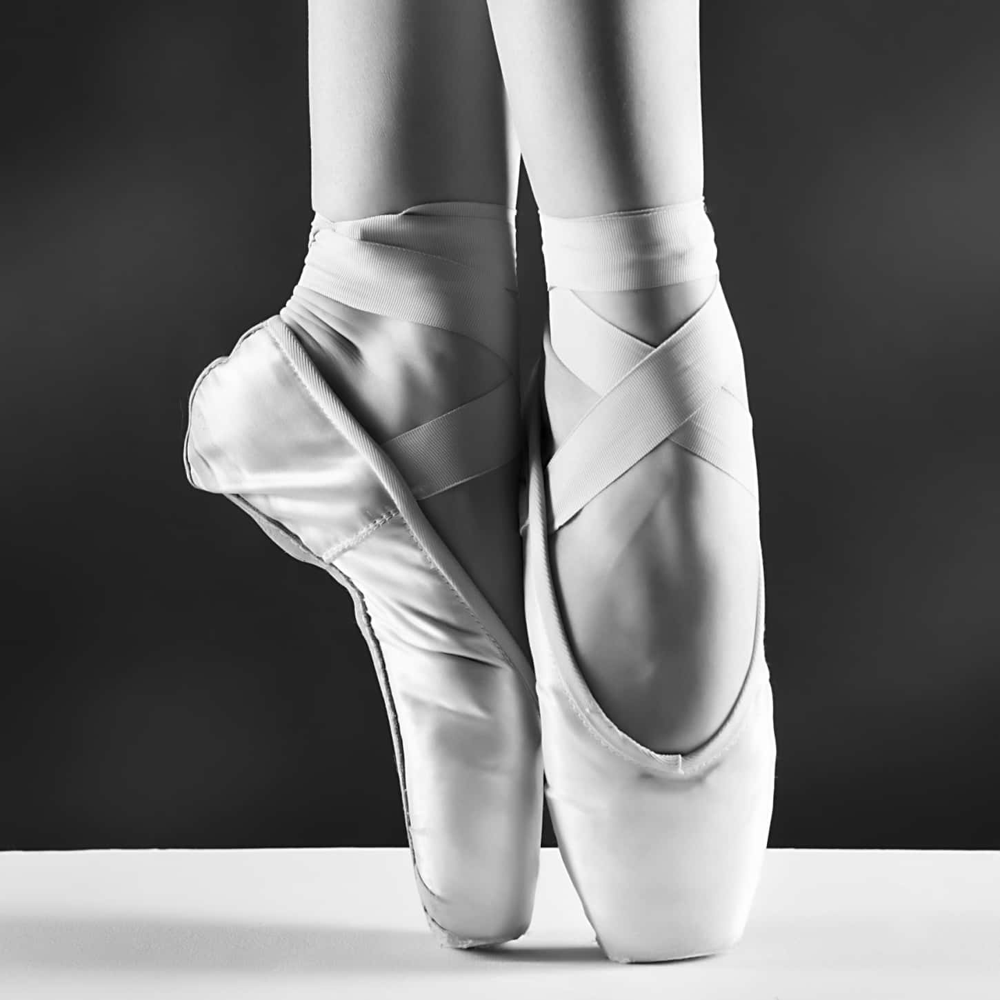 ballerina 桌布 壁紙 — 芭蕾舞者穿著足尖鞋的腳部黑白特寫，優雅地擺放在白色表面上，背景為深色漸變。