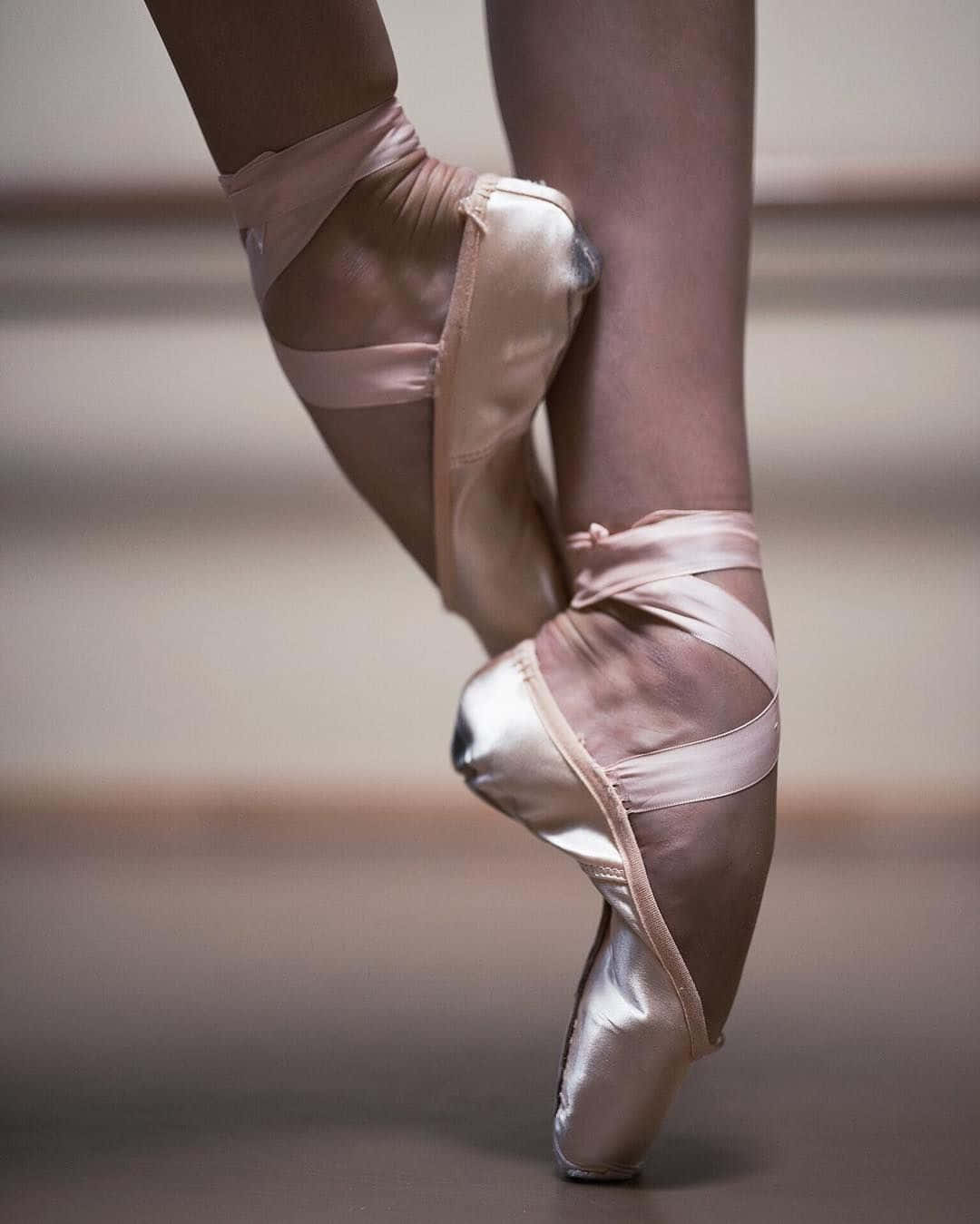 Ballet 桌布 壁紙 — 芭蕾舞者雙腳穿著淡粉紅色緞面足尖鞋，在舞蹈室地板上優雅地以足尖平衡的特寫。
