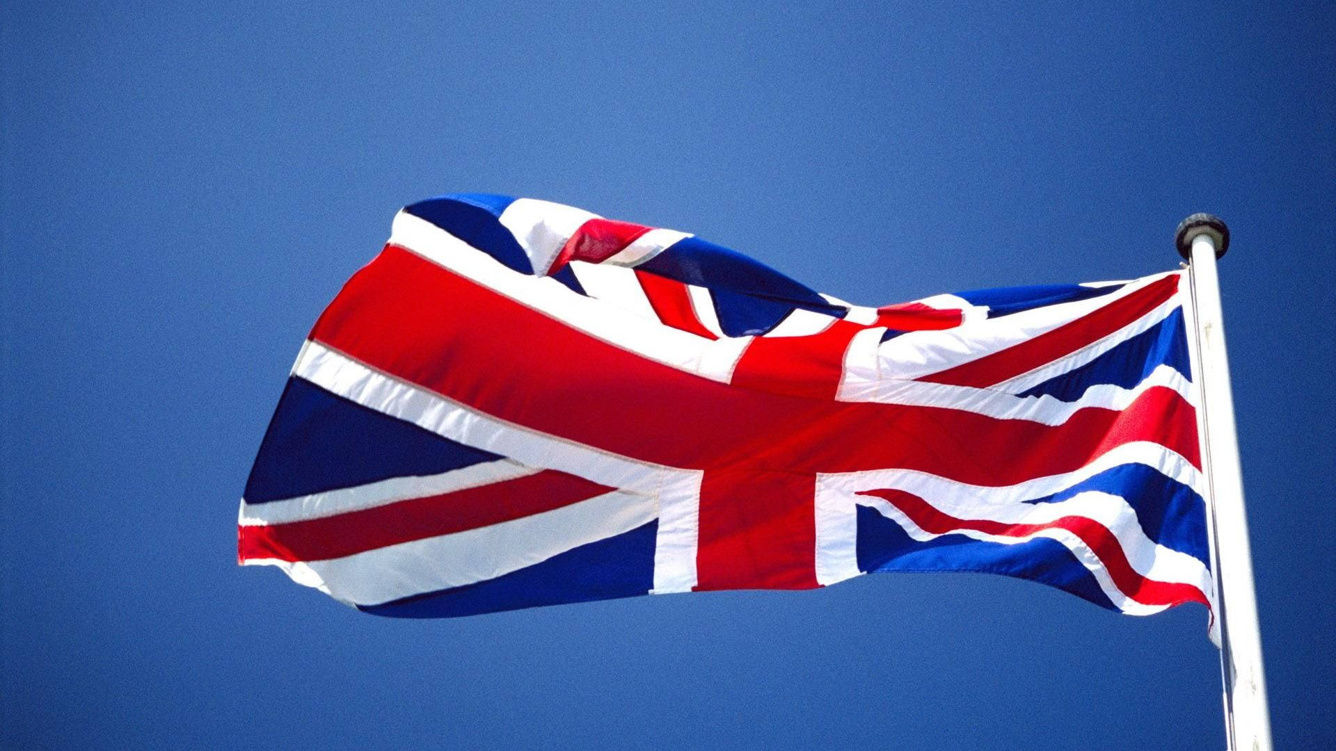 United Kingdom Flag 桌布 壁紙 — 英國國旗在晴朗的日子裡，在清澈的藍天下動態飄揚。