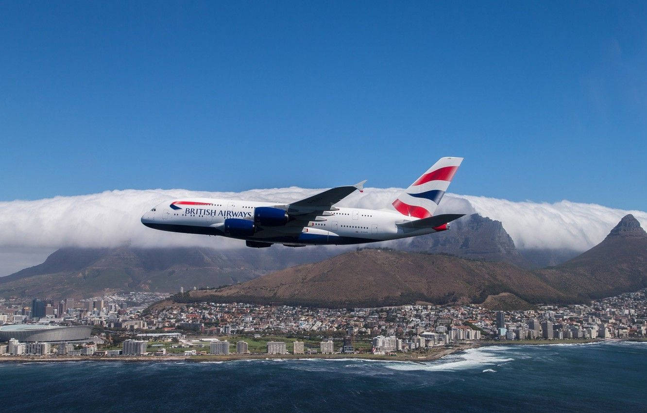 雲朵 桌布 壁紙 — 英國航空的空中巴士A380在晴朗藍天下翱翔於沿海城市上空，下方有山脈和雲層。