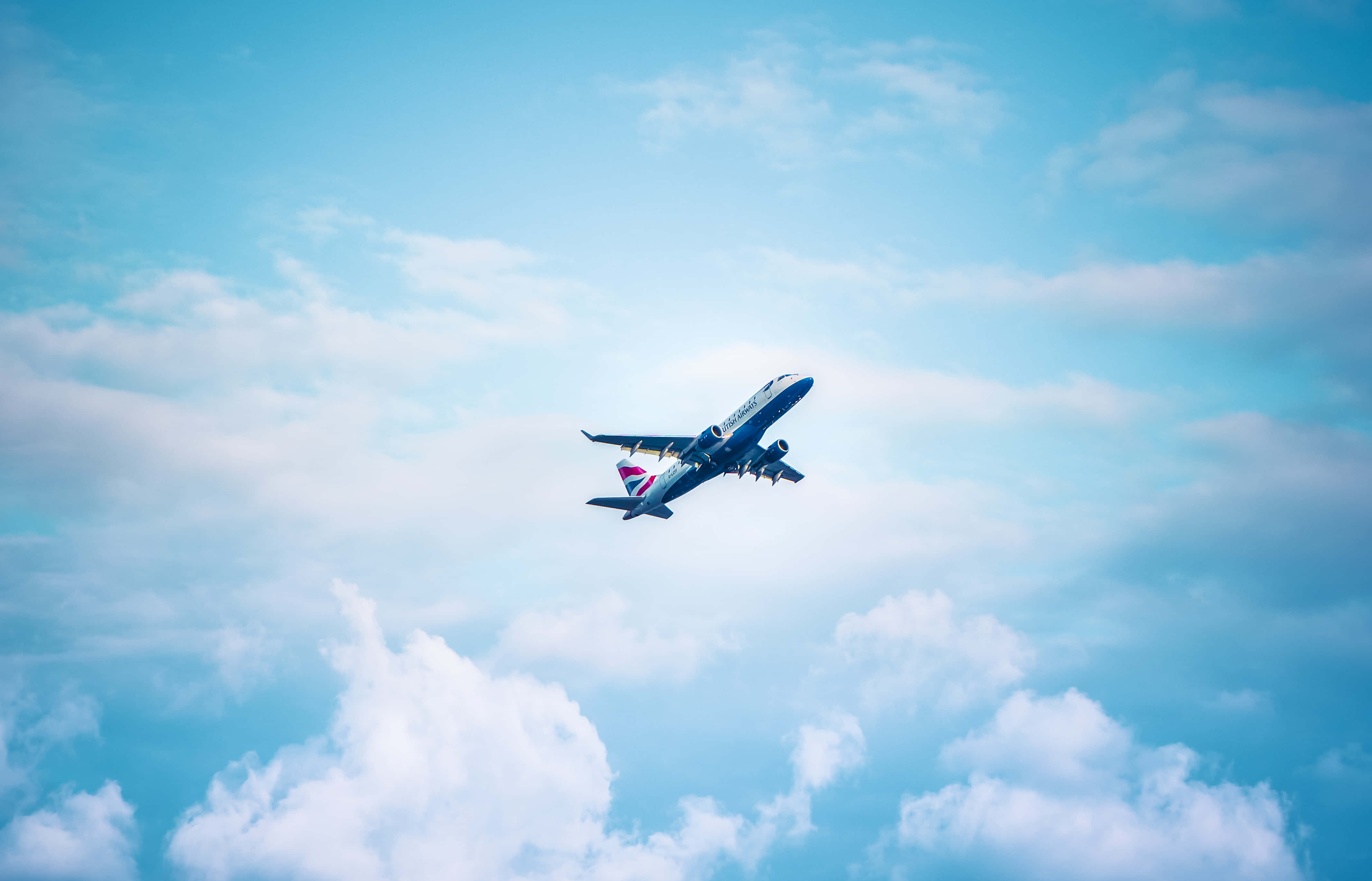 Plane Desktop 桌布 壁紙 — 英國航空飛機在鮮豔的藍天背景下優雅地翱翔於蓬鬆的白雲之上。