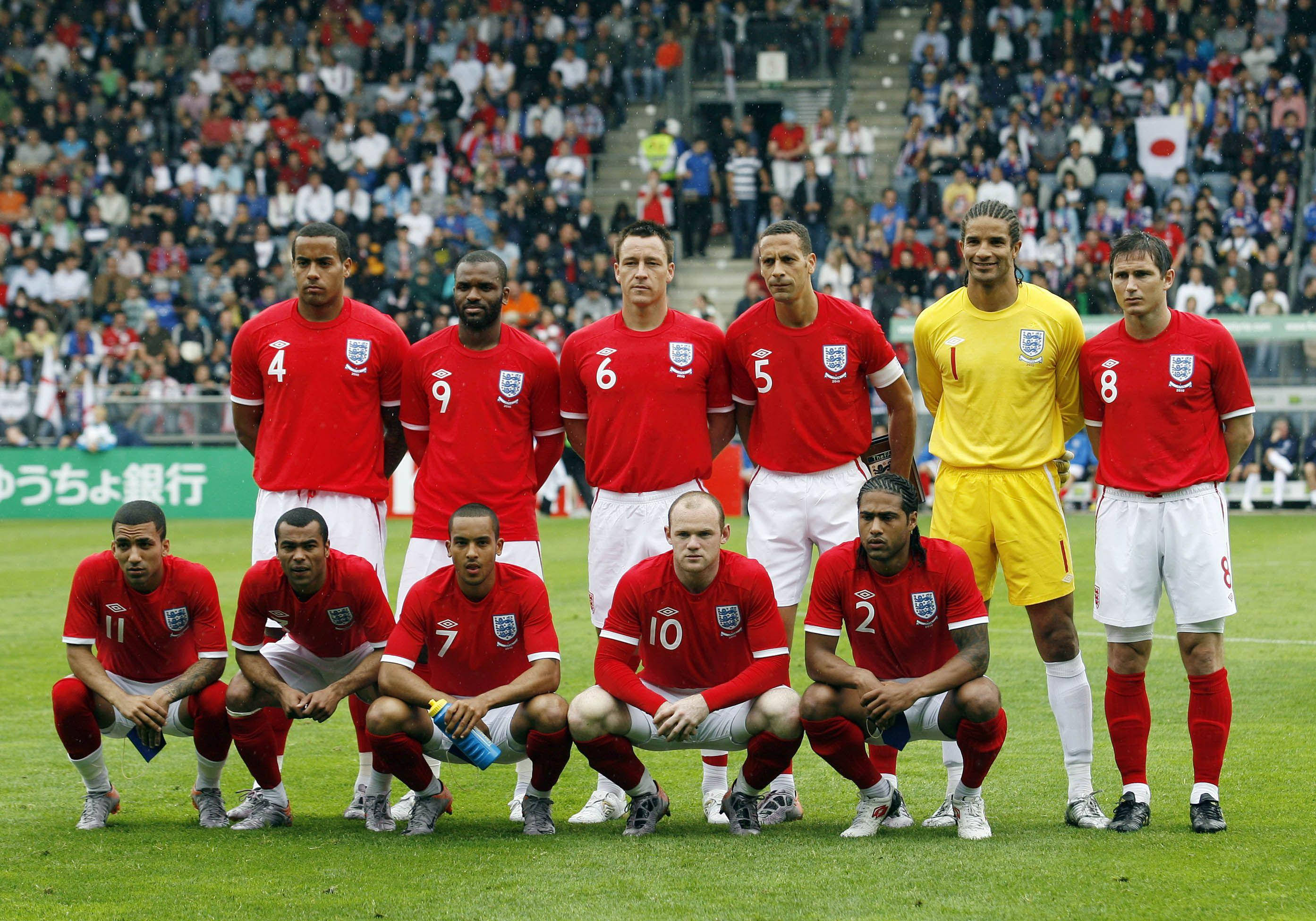 Football Players 桌布 壁紙 — 英格蘭國家足球隊在陰天、座無虛席的球場前，身穿紅色球衣在綠色草地上擺姿勢。