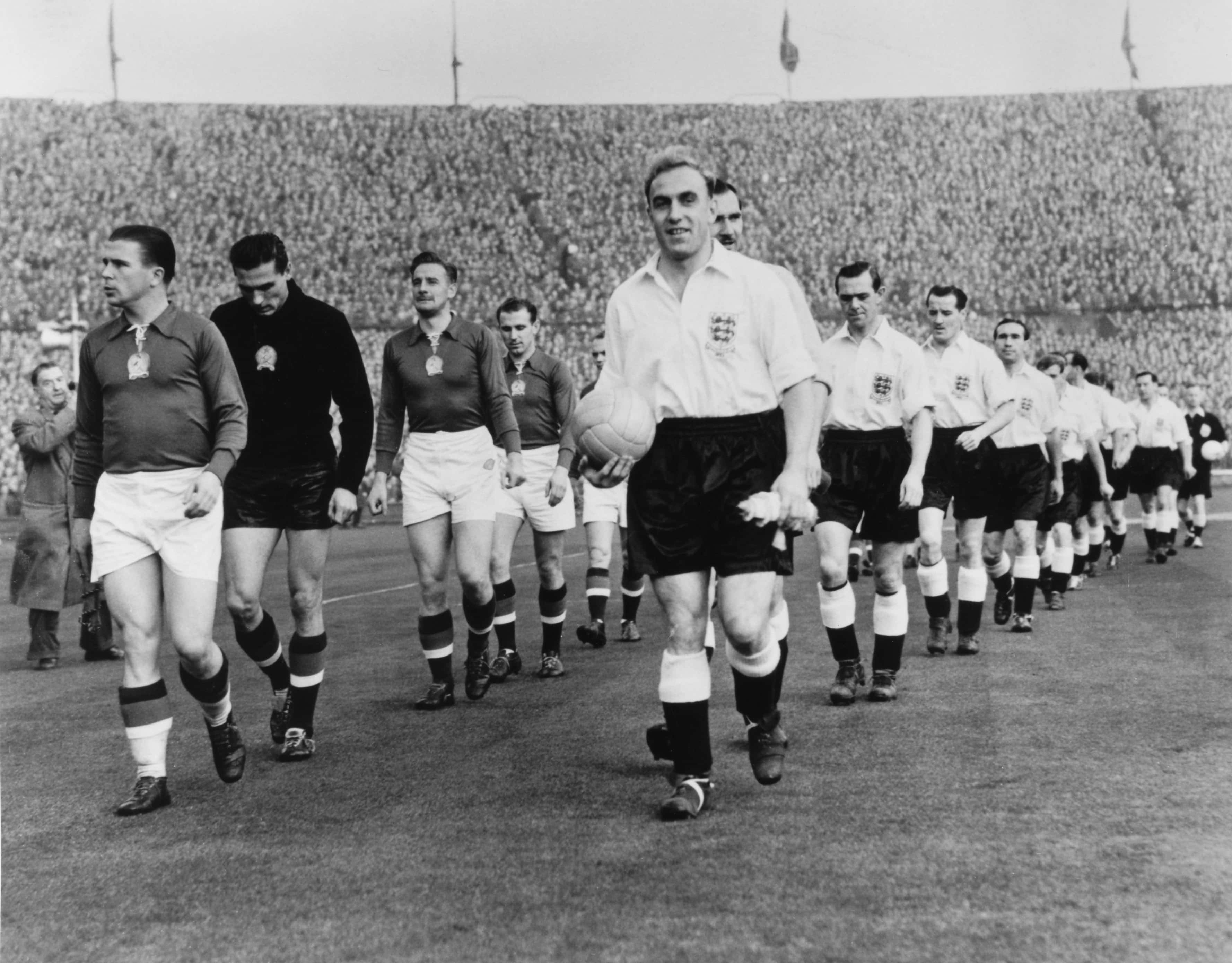 Football Players 桌布 壁紙 — 英格蘭橄欖球隊手持球走進球場，背景有體育場觀眾的復古黑白照片。