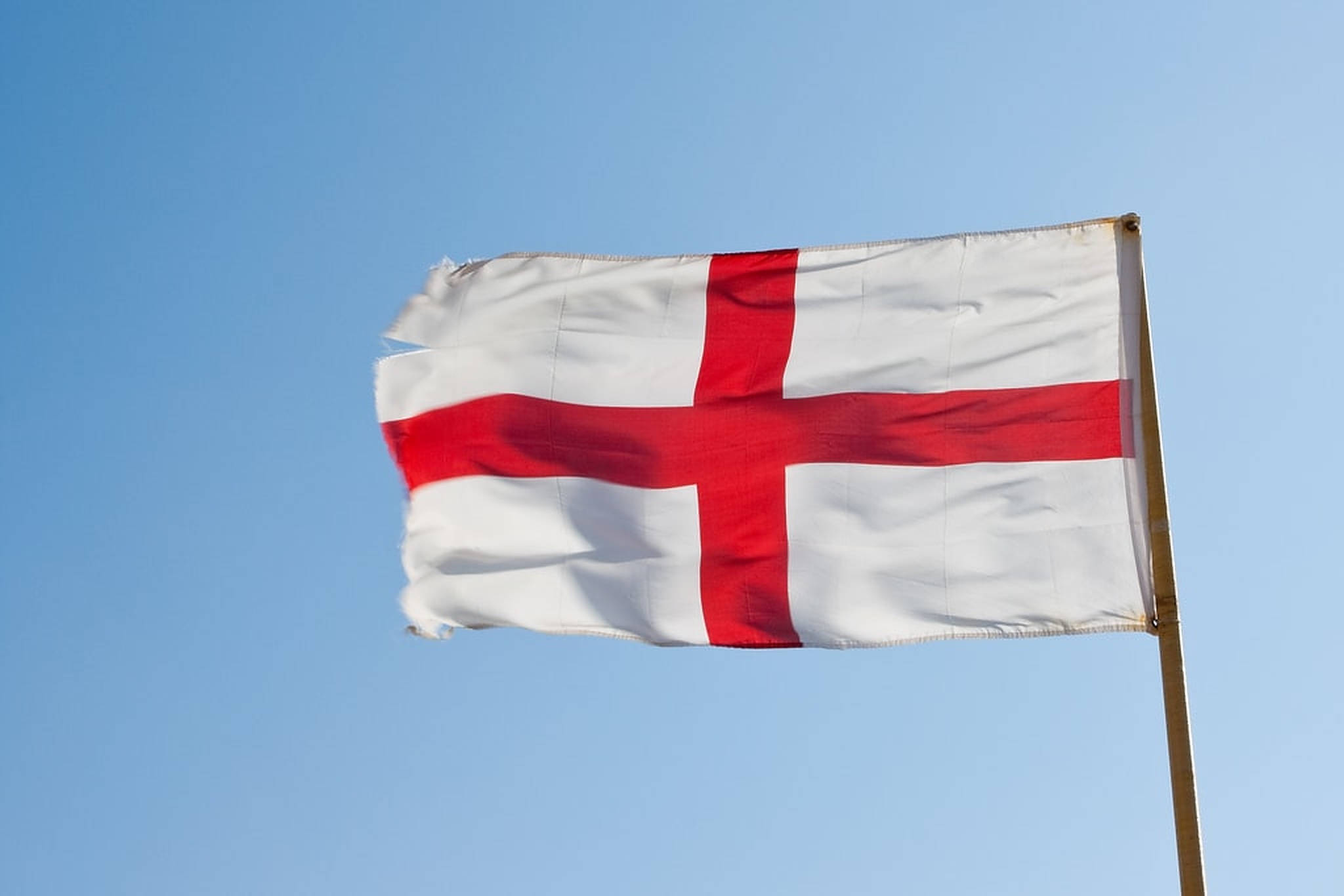 England Flag 桌布 壁紙 — 英格蘭的聖喬治十字旗在晴朗的日子裡，在清澈的藍天下自豪地飄揚。
