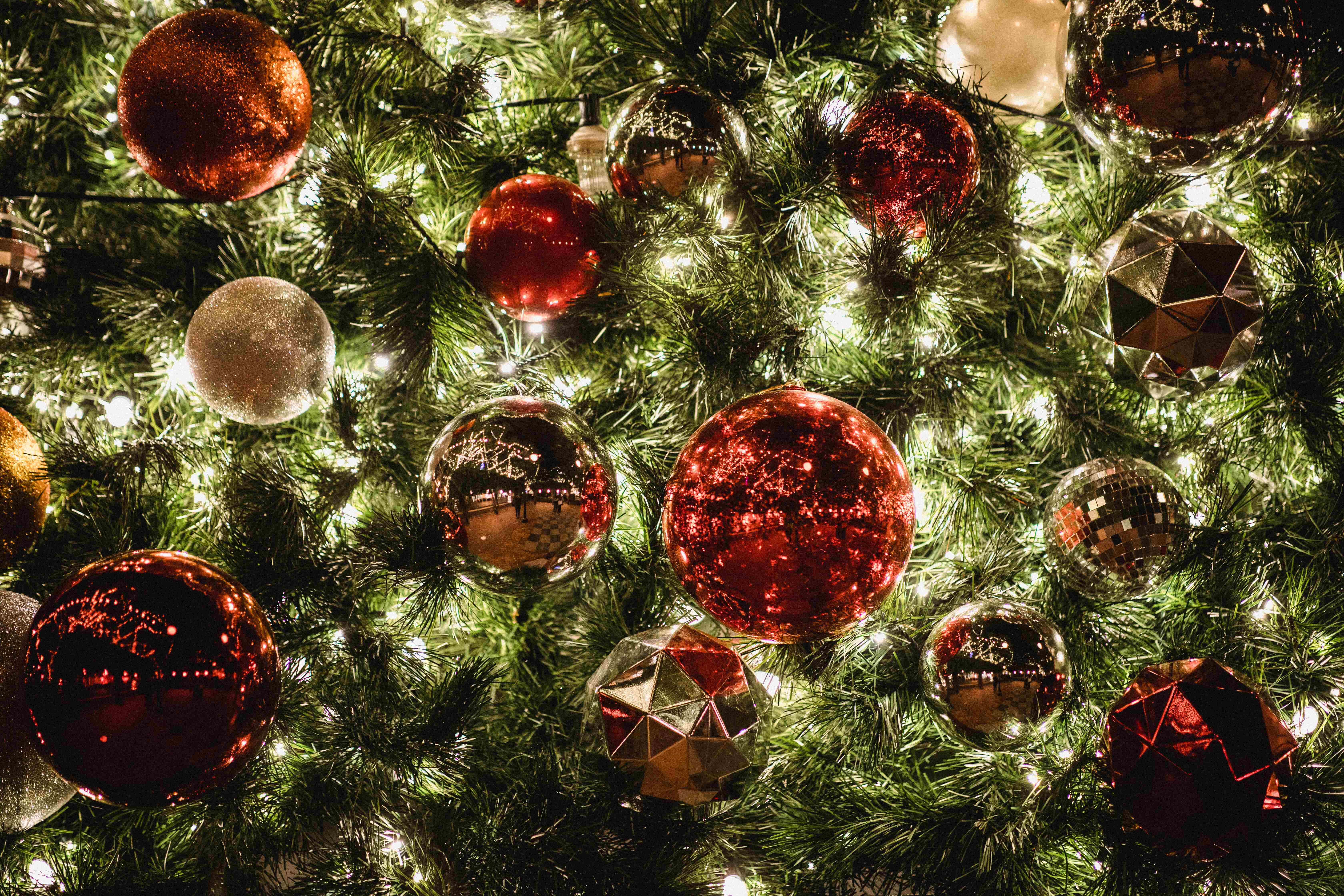 Christmas Scene 桌布 壁紙 — 茂密綠色聖誕樹的特寫，裝飾著閃閃發光的紅色和銀色飾品以及溫暖閃爍的燈光。