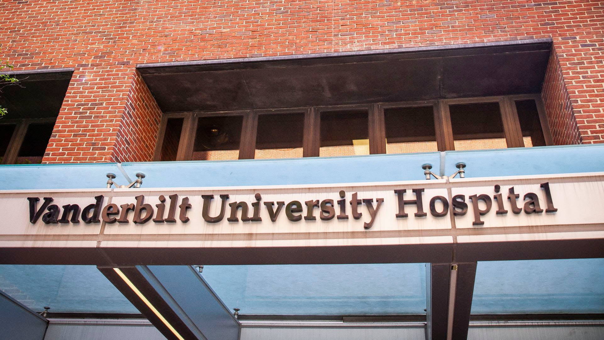 Hospital 桌布 壁紙 — 范德比爾特大學醫院標誌的特寫，安裝在帶有玻璃和金屬遮陽篷的紅磚建築上。