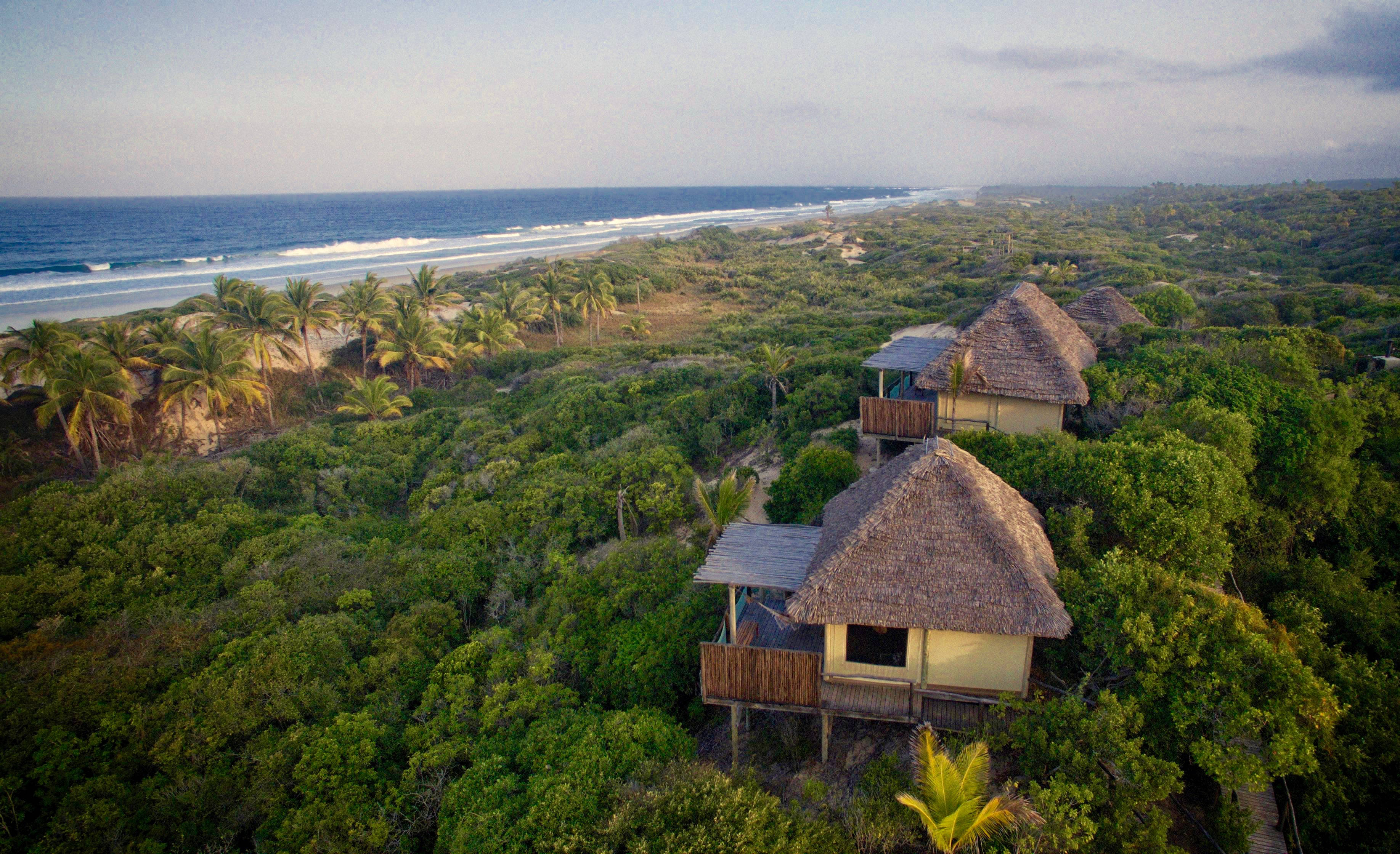 Mozambique 桌布 壁紙 — 茅草屋頂小屋的鳥瞰圖，坐落在鬱鬱蔥蔥的綠色叢林中，旁邊是碧綠色的海洋，海浪輕柔。