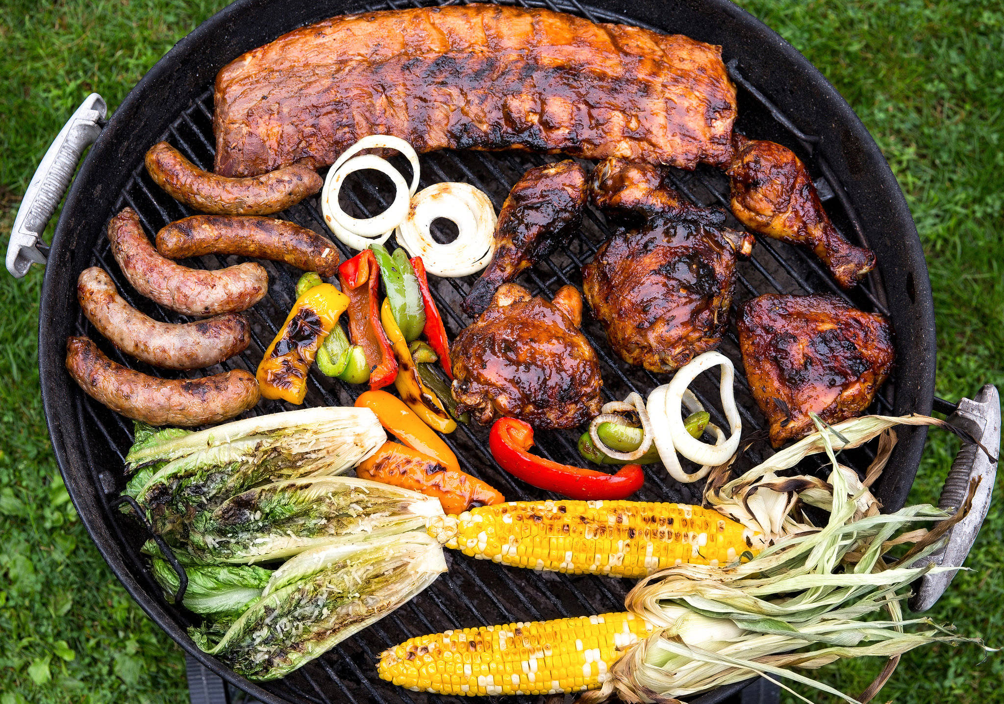 meat 桌布 壁紙 — 草地上一個滋滋作響的燒烤架，放滿肋骨、香腸、雞肉、玉米和甜椒。
