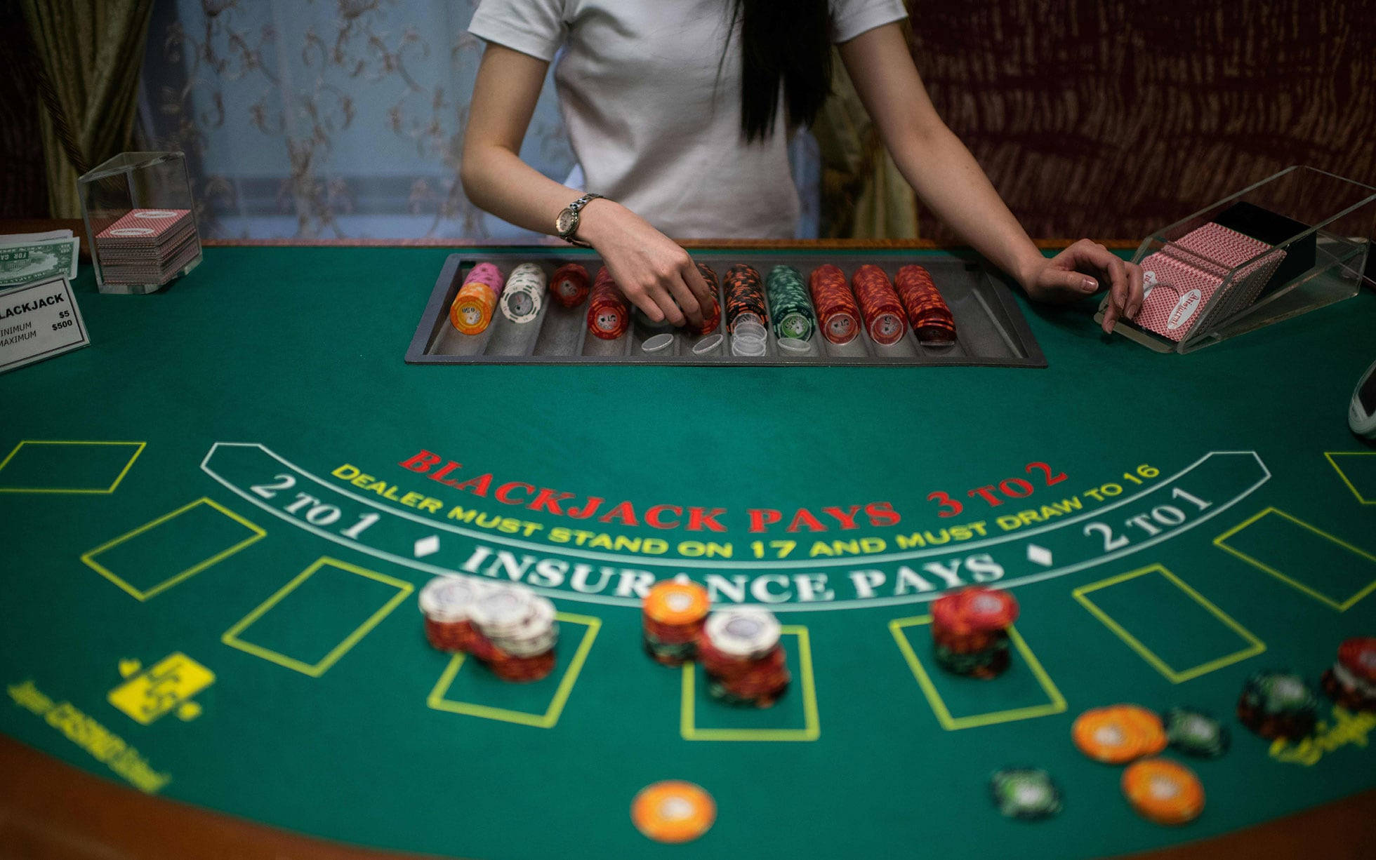 Casino 桌布 壁紙 — 荷官在綠色二十一點桌上排列彩色籌碼，桌上印有規則，並散落著一堆堆籌碼。