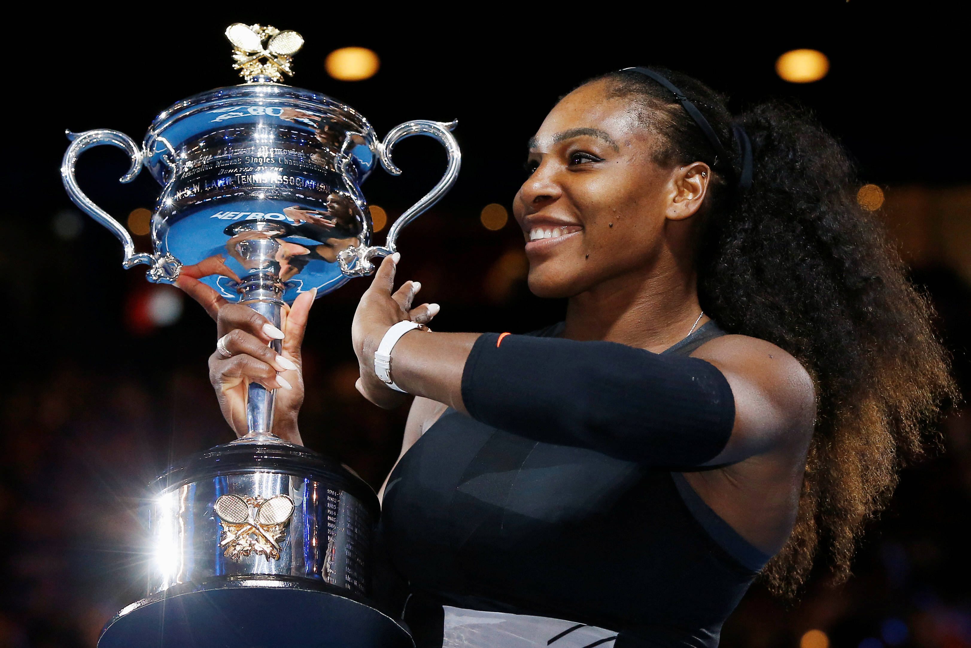 Serena 桌布 壁紙 — 莎蓮娜威廉絲在明亮的體育場燈光下自豪地閃耀著，手持閃閃發光的溫布頓獎盃。