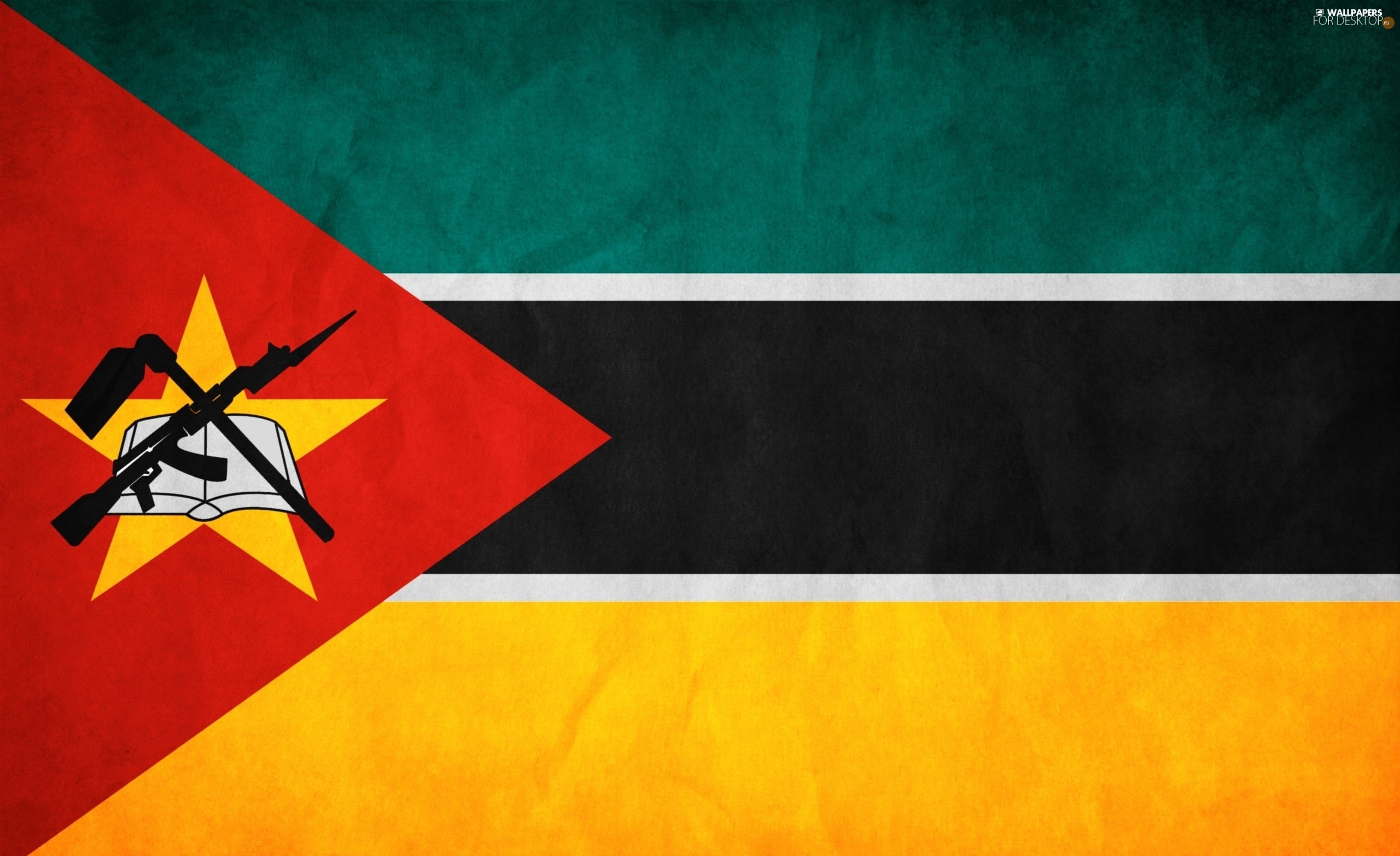 Mozambique 桌布 壁紙 — 莫三比克國旗的紋理壁紙，帶有紅色、綠色、黑色和黃色條紋，以及中央的交叉步槍放在打開的書本上，位於黃色星星上的標誌。