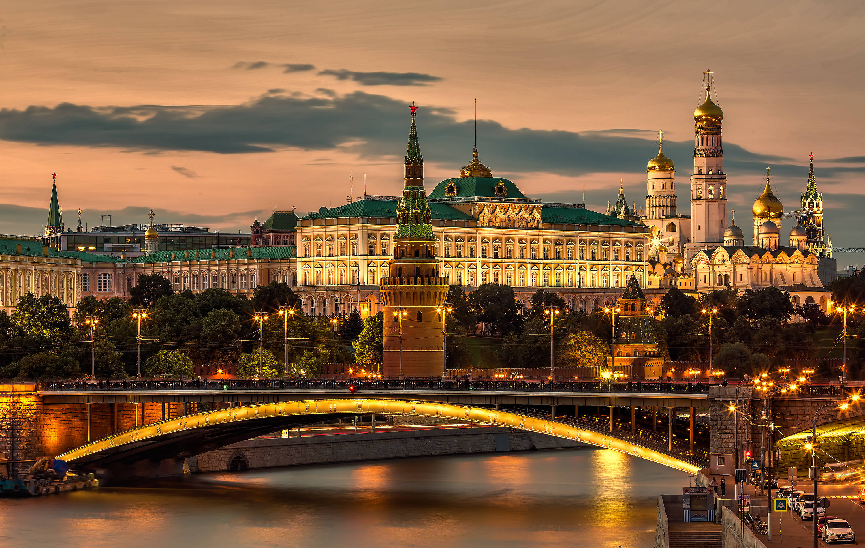 Russia 桌布 壁紙 — 莫斯科克里姆林宮的金色圓頂和尖塔在暮色中溫暖地發光，下方一座燈火通明的橋樑橫跨河流。