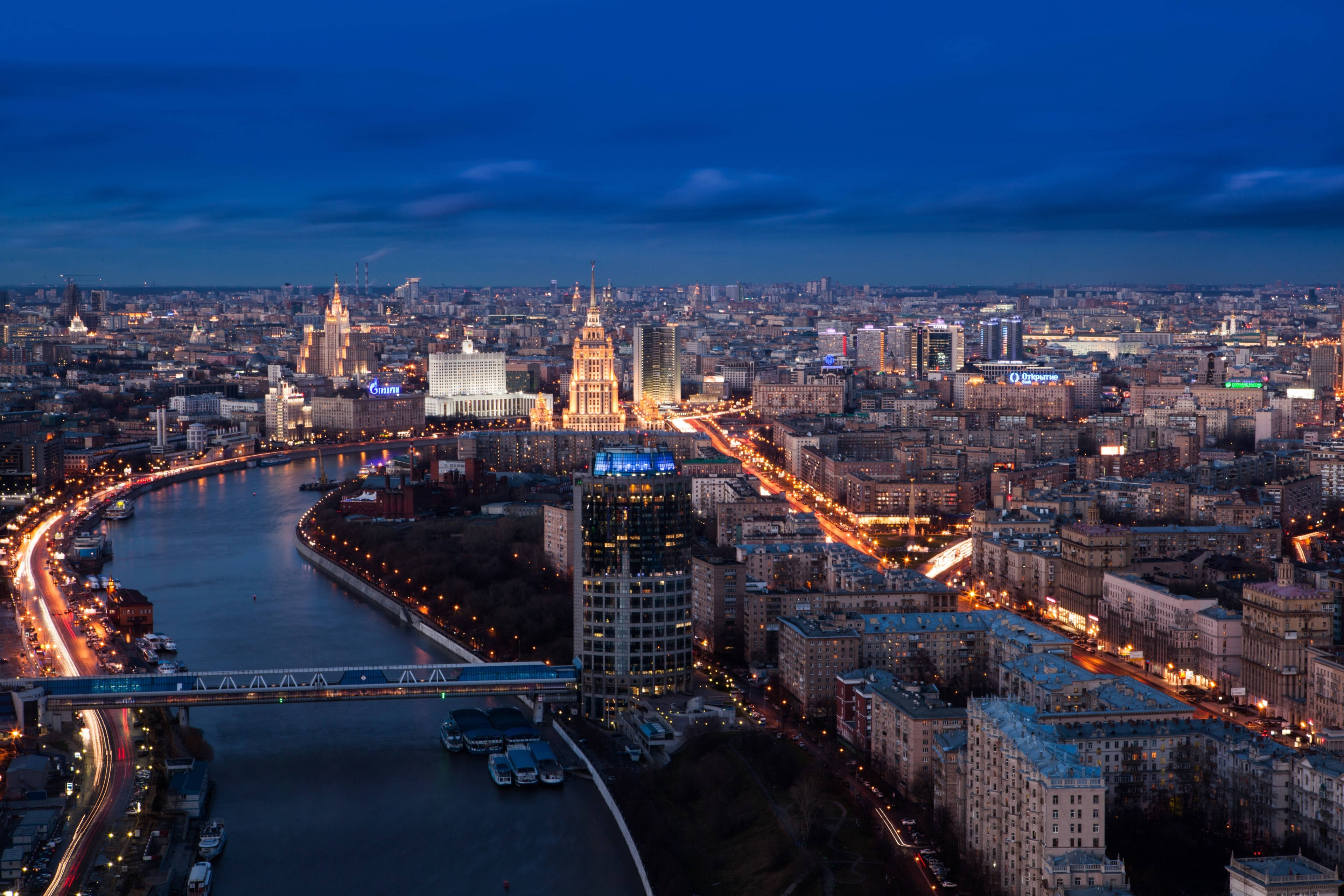 Moscow 桌布 壁紙 — 莫斯科黃昏時的鳥瞰圖，河流沿岸閃爍的城市燈光以及標誌性摩天大樓在深藍色天空映襯下的剪影。