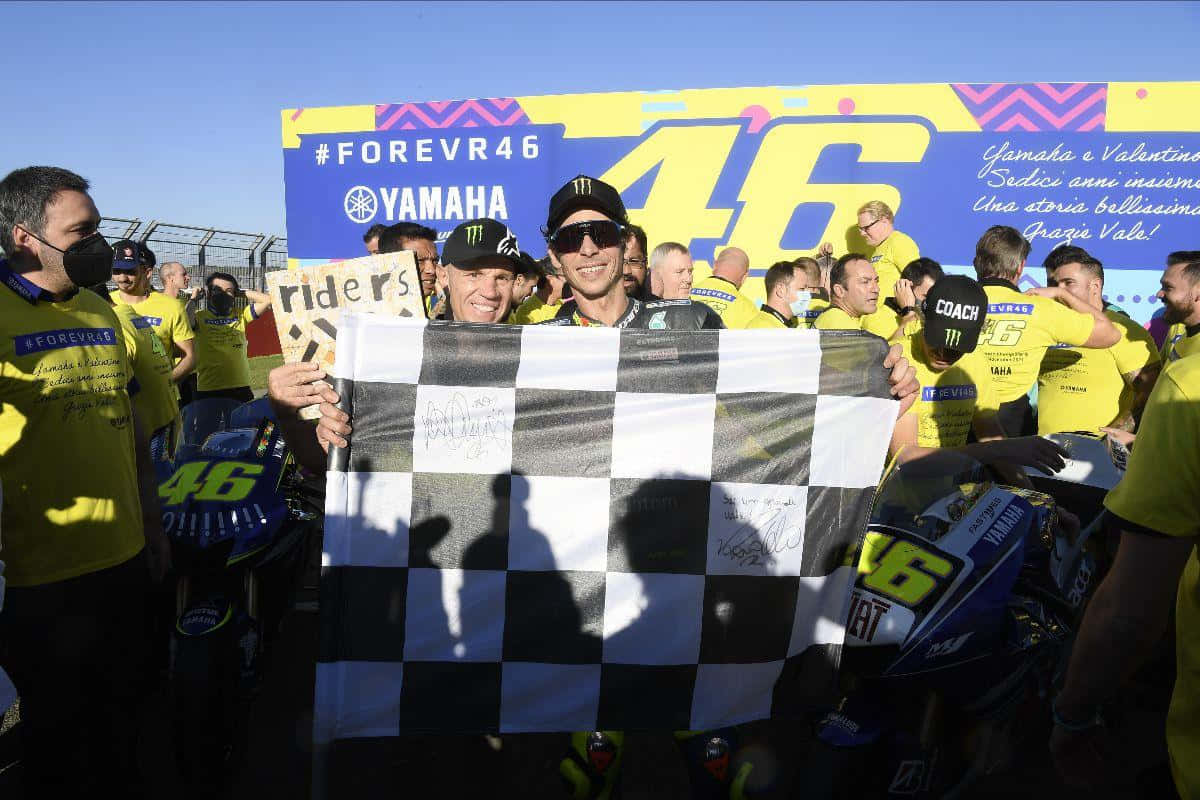 Chequered Flag 桌布 壁紙 — 華倫天奴·羅西在燦爛陽光下與舉著格子旗的粉絲和車隊慶祝勝利。