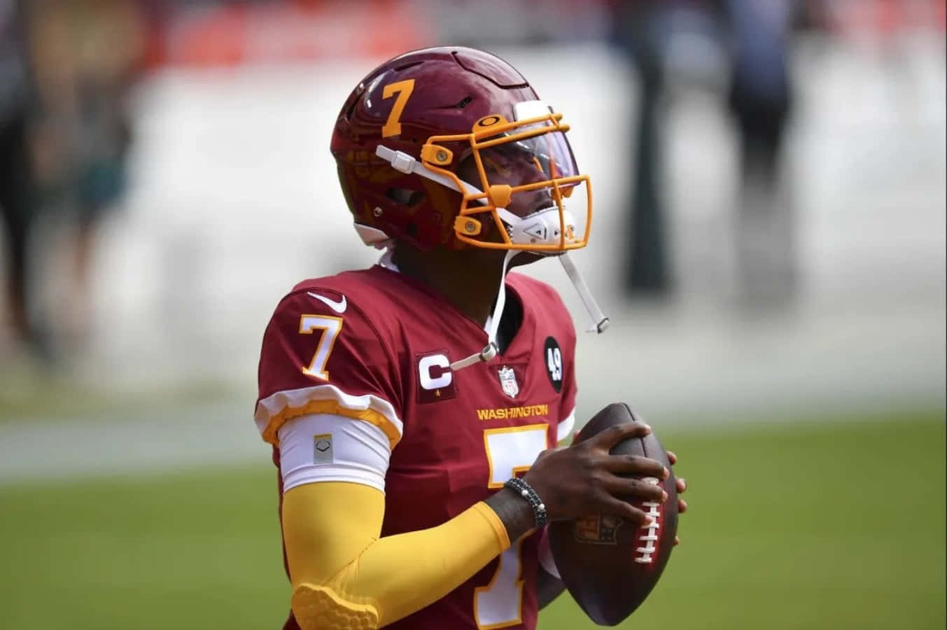 Washington Football 桌布 壁紙 — 華盛頓美式足球隊的四分衛身穿栗色和金色球衣，在陽光明媚的比賽日於綠色球場上手持美式足球。