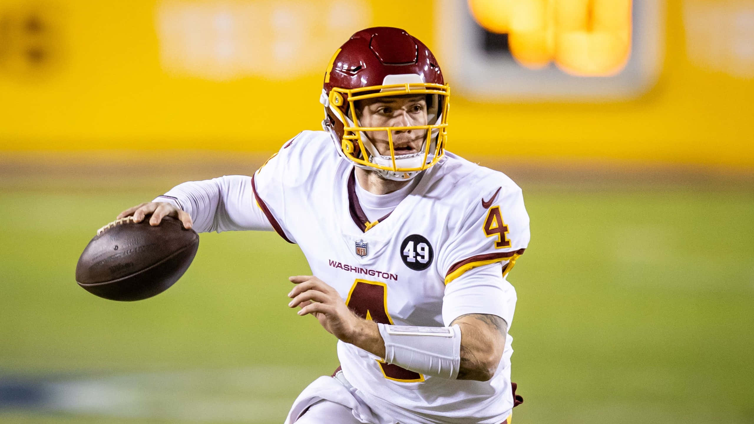 Dwayne Haskins 桌布 壁紙 — 華盛頓美式足球隊的四分衛身穿白色和酒紅色制服，在夜間比賽中於體育館燈光下投擲美式足球。