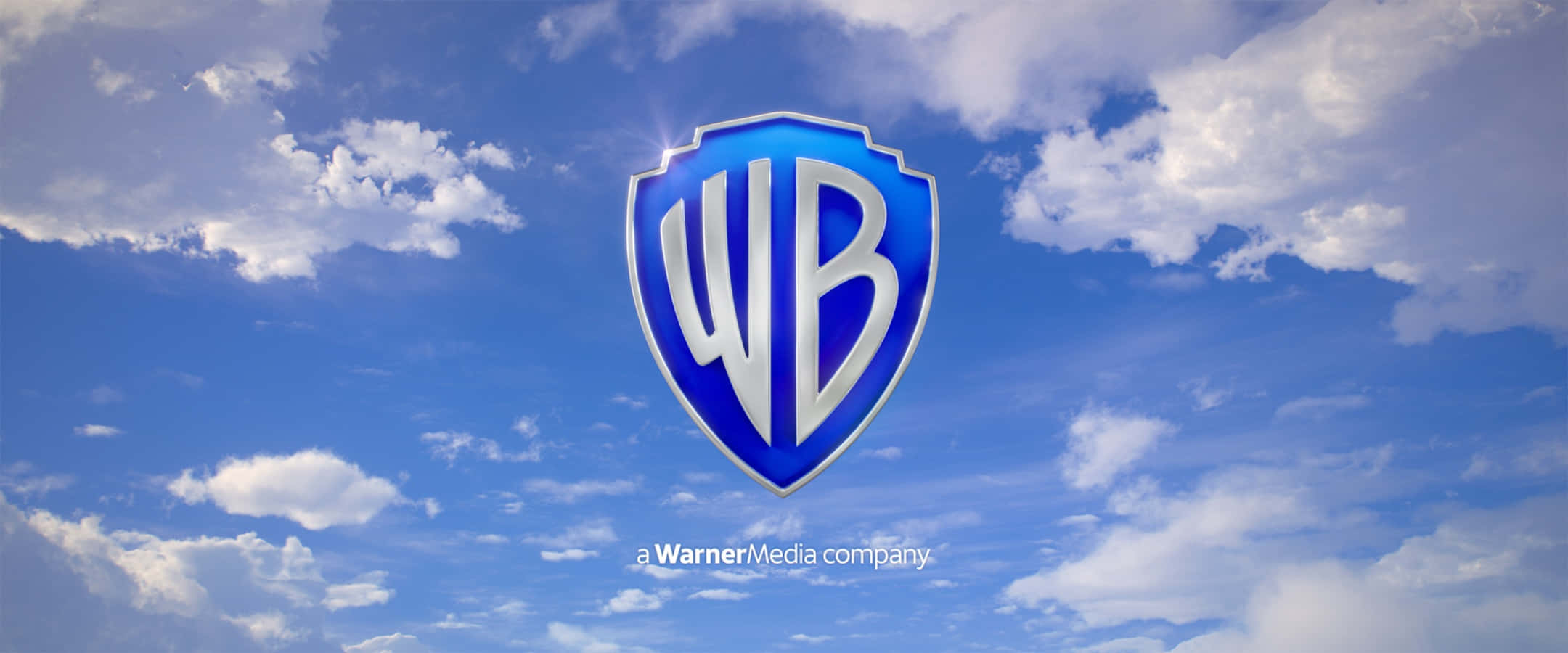 Warner Bros 桌布 壁紙 — 華納兄弟的盾牌標誌在點綴著蓬鬆白雲的明亮藍天中閃耀。