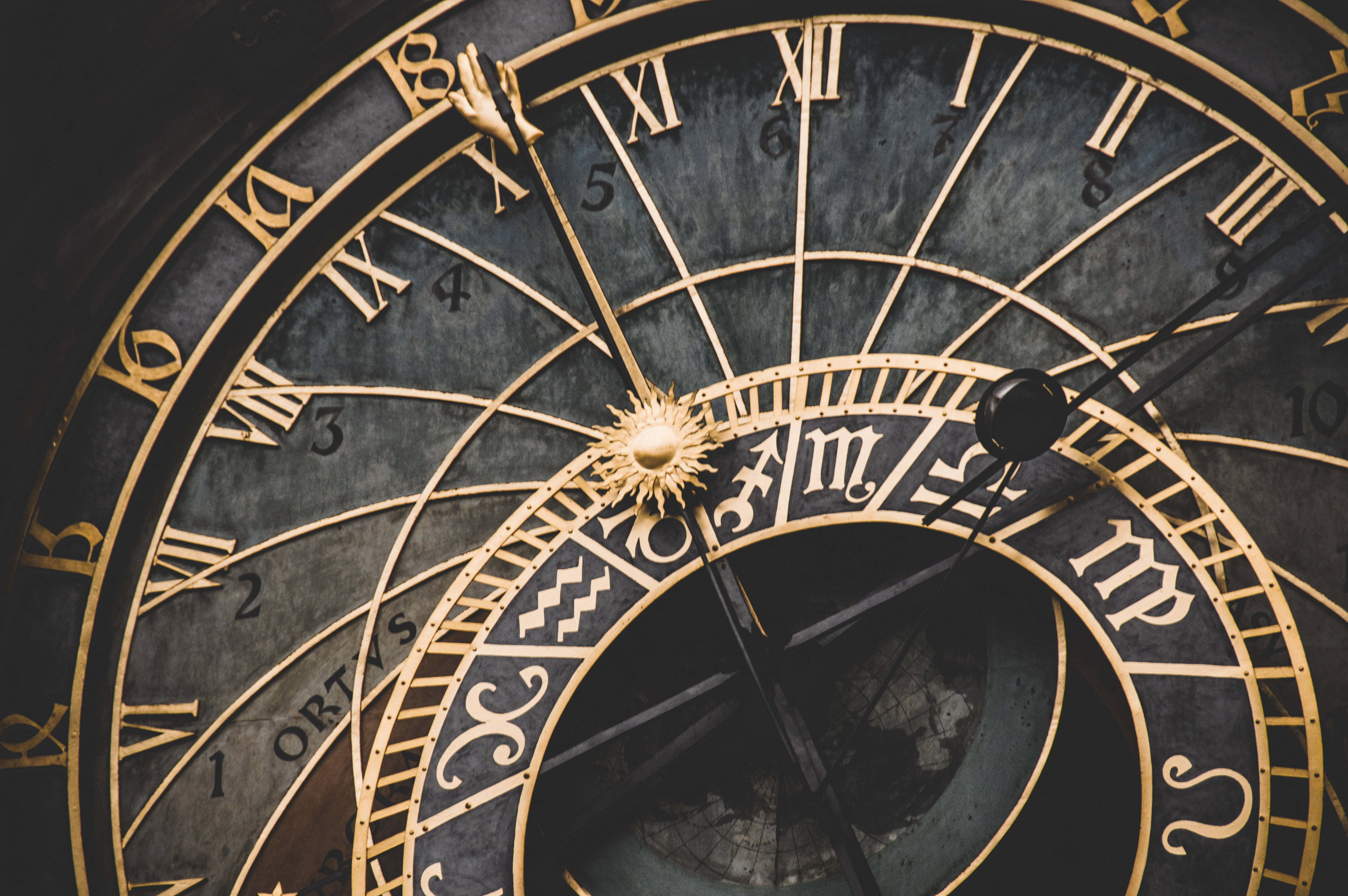 zodiac 桌布 壁紙 — 華麗天文鐘的特寫，帶有金色羅馬數字、星座符號和複雜齒輪，背景為深色石頭。