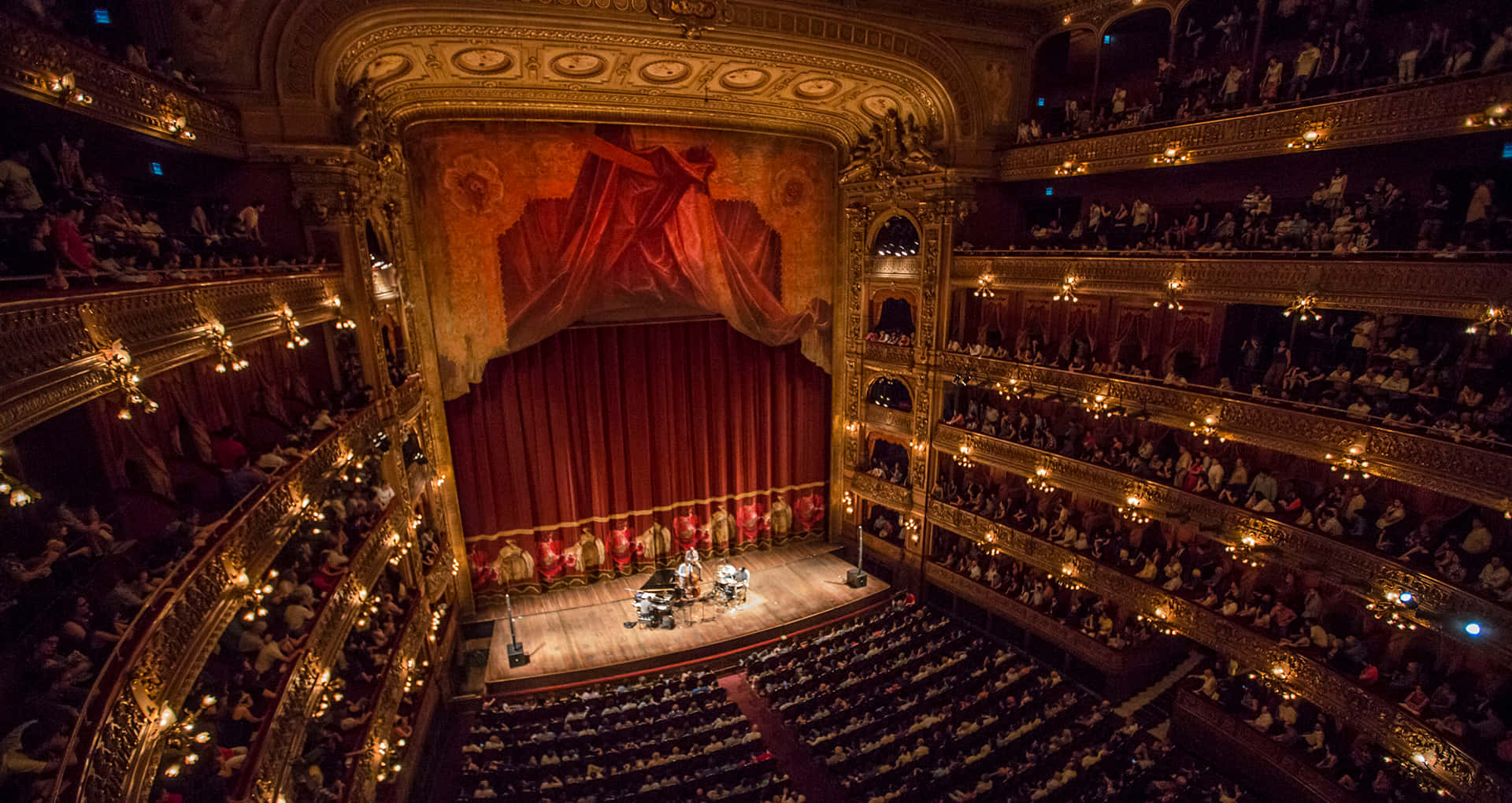 theatre 桌布 壁紙 — 華麗宏偉的劇院，觀眾在溫暖的金色燈光下觀看表演，座無虛席。