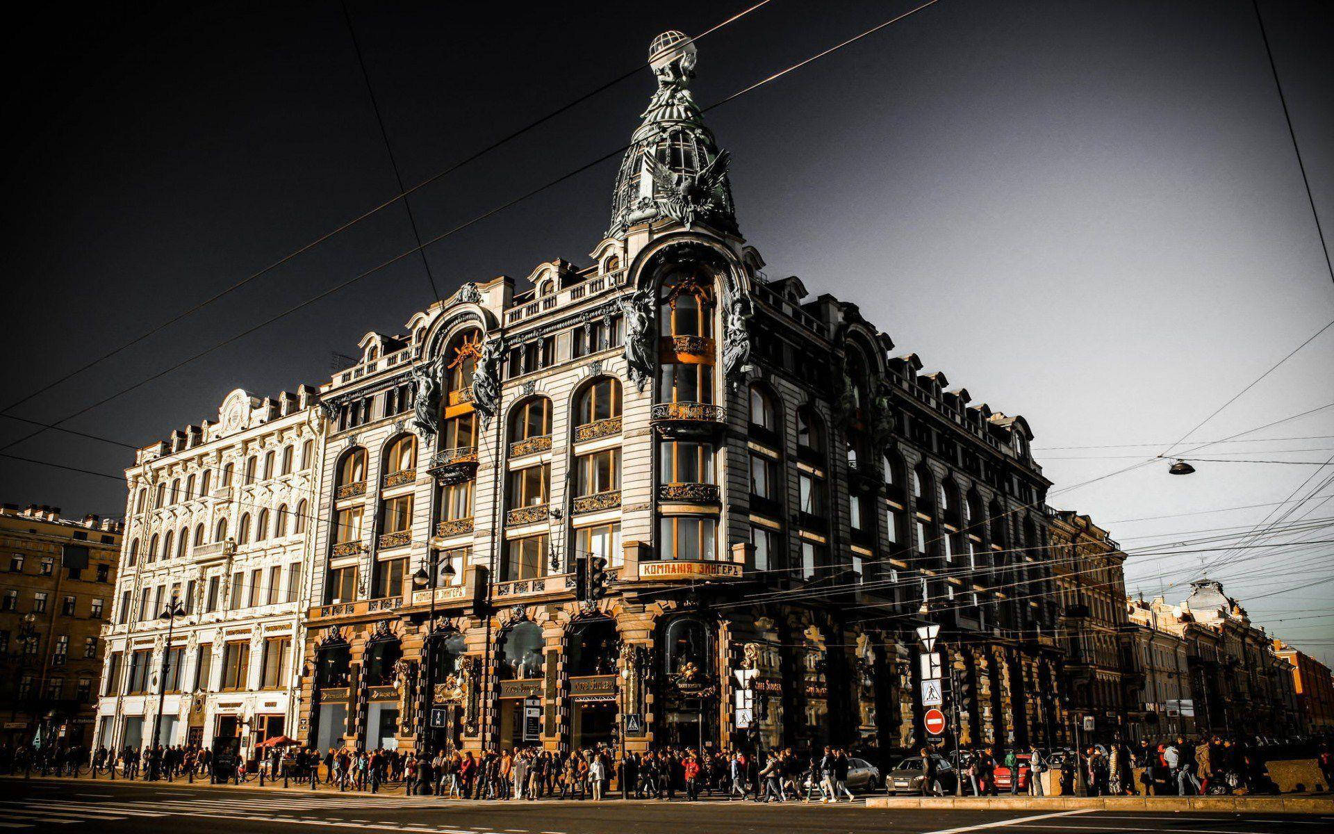 Saint Petersburg 桌布 壁紙 — 華麗的裝飾建築，擁有複雜的外牆和金色點綴，矗立在街角，黃昏天空下，下方人群熙攘。