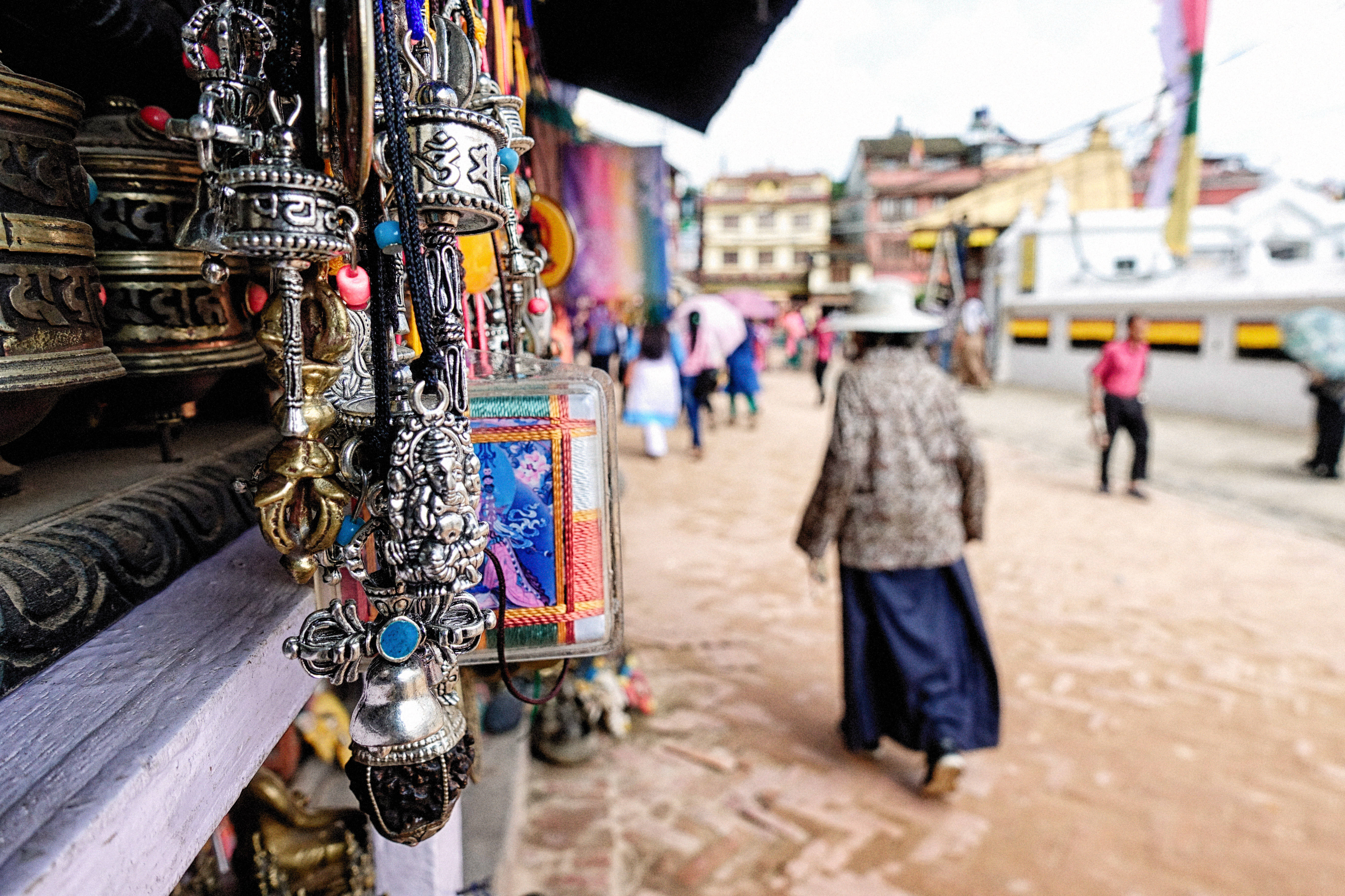 Nepal 桌布 壁紙 — 華麗的西藏轉經輪和小飾品在攤位上的特寫，背景有模糊的行人走在鵝卵石街道上。