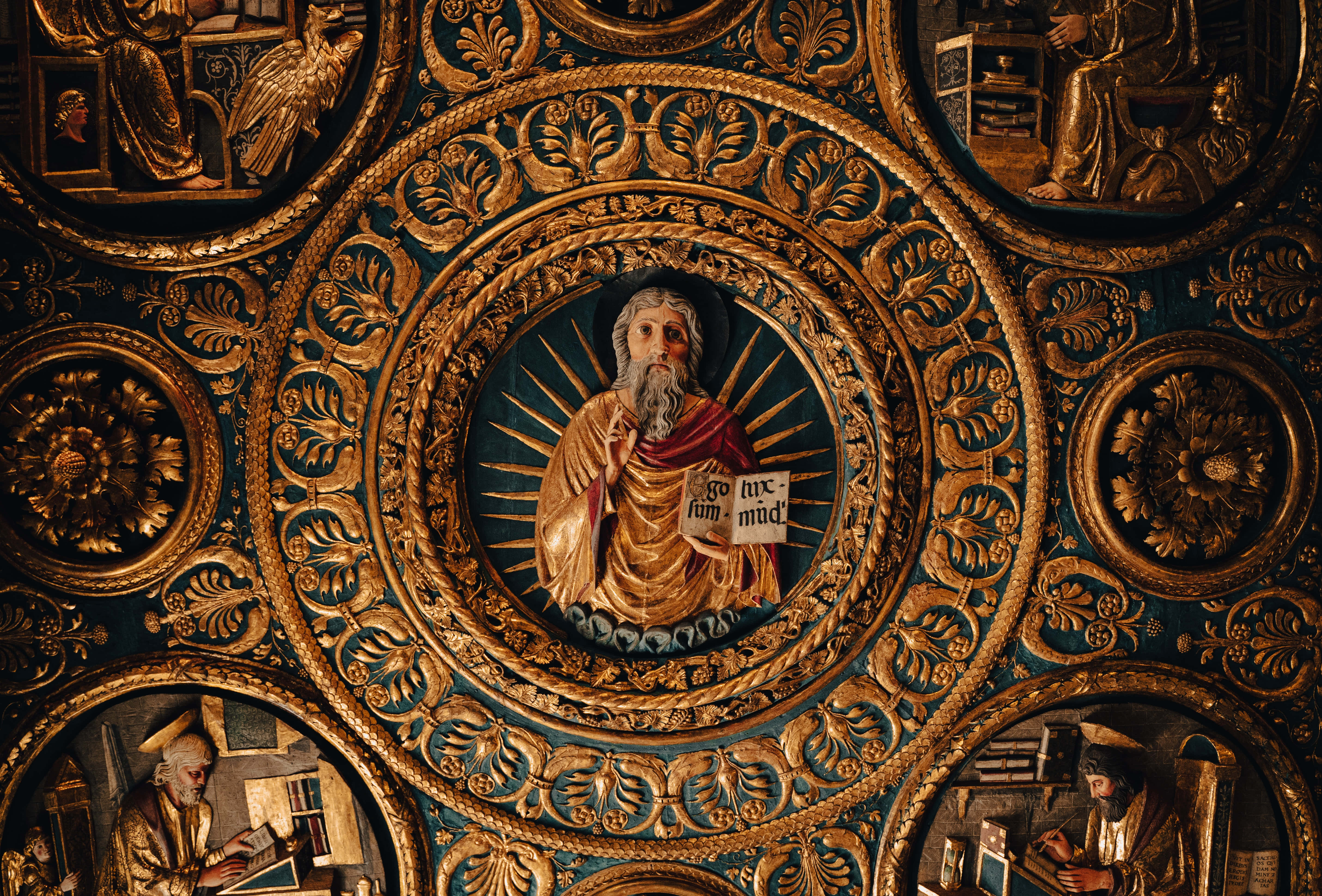 Religious Art 桌布 壁紙 — 華麗的金色宗教天花板壁畫，中央有一位留鬍鬚的聖人，在深藍色背景前手持卷軸。