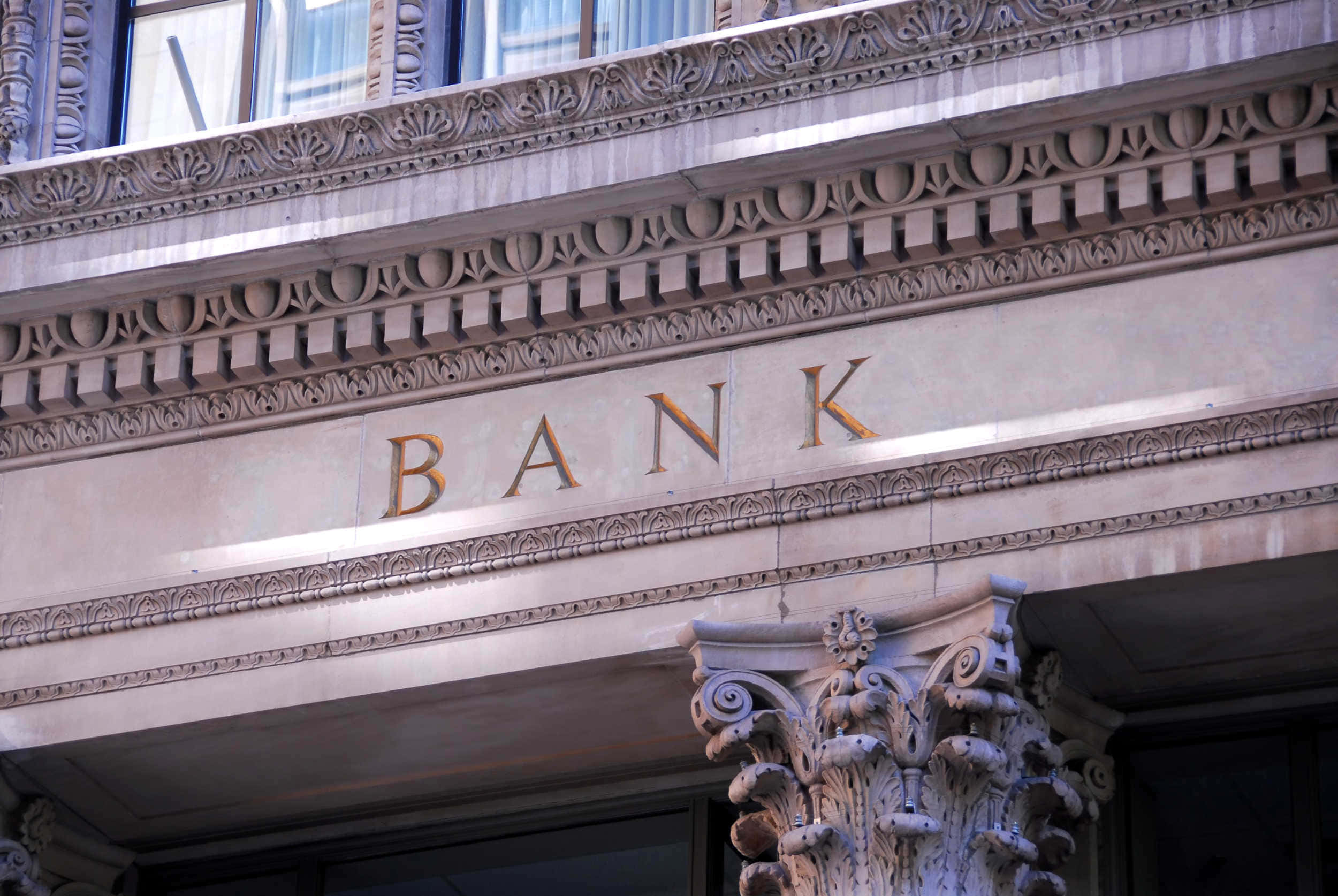 Bank 桌布 壁紙 — 華麗石造銀行大樓正面的特寫，帶有精緻雕刻和金色字母拼出BANK。