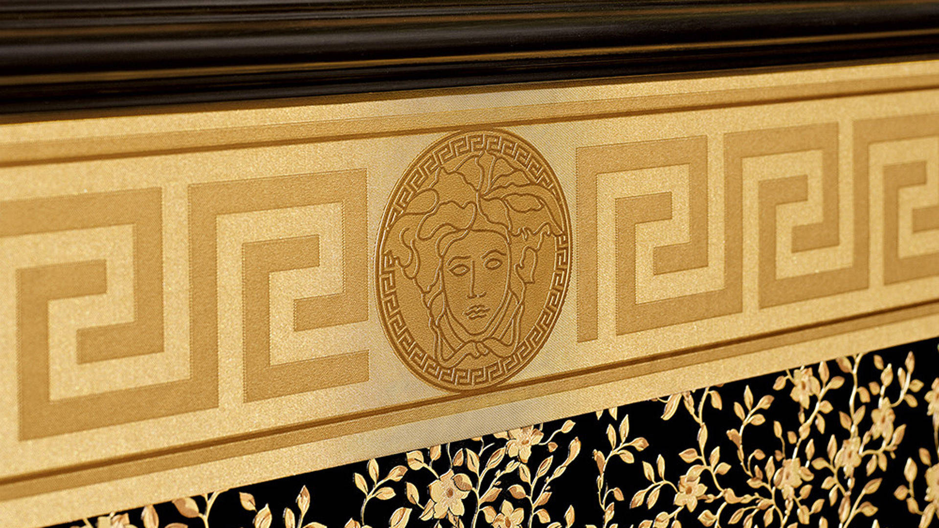 Versace Logo 桌布 壁紙 — 華麗金色希臘鑰匙圖案的特寫，帶有美杜莎頭像獎章，鑲嵌在黑色花卉圖案中。