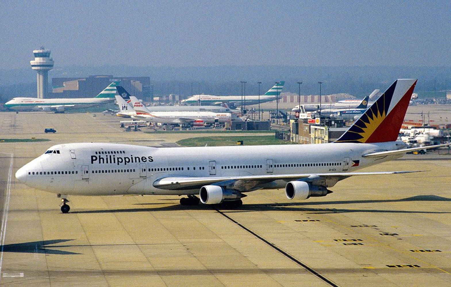 Airport 桌布 壁紙 — 菲律賓航空一架波音747在陽光明媚的機場停機坪上滑行，背景有其他飛機和控制塔。