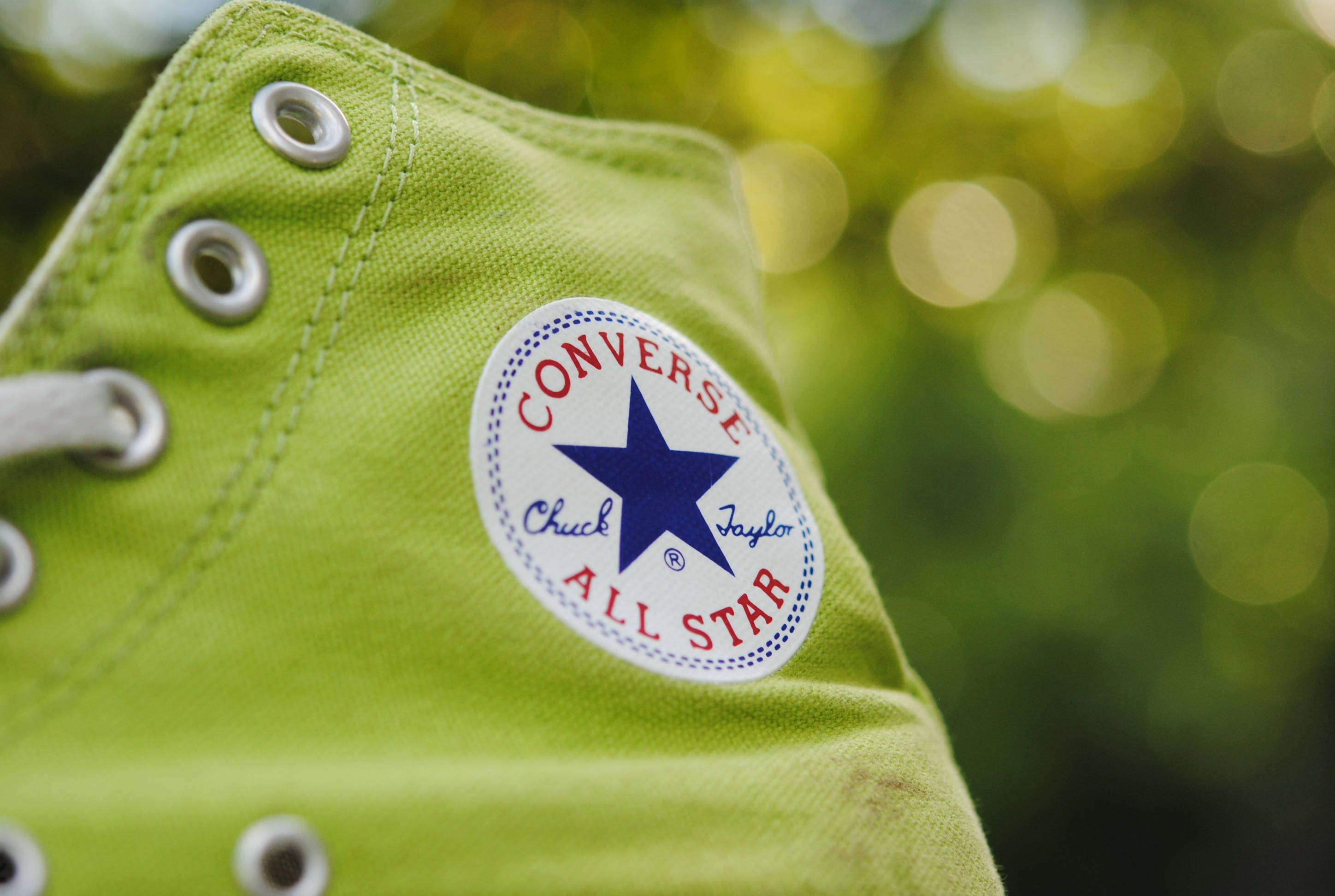 Converse 桌布 壁紙 — 萊姆綠色Converse Chuck Taylor All Star運動鞋特寫，配有白色鞋帶和銀色鞋眼，背景為模糊的綠色散景。