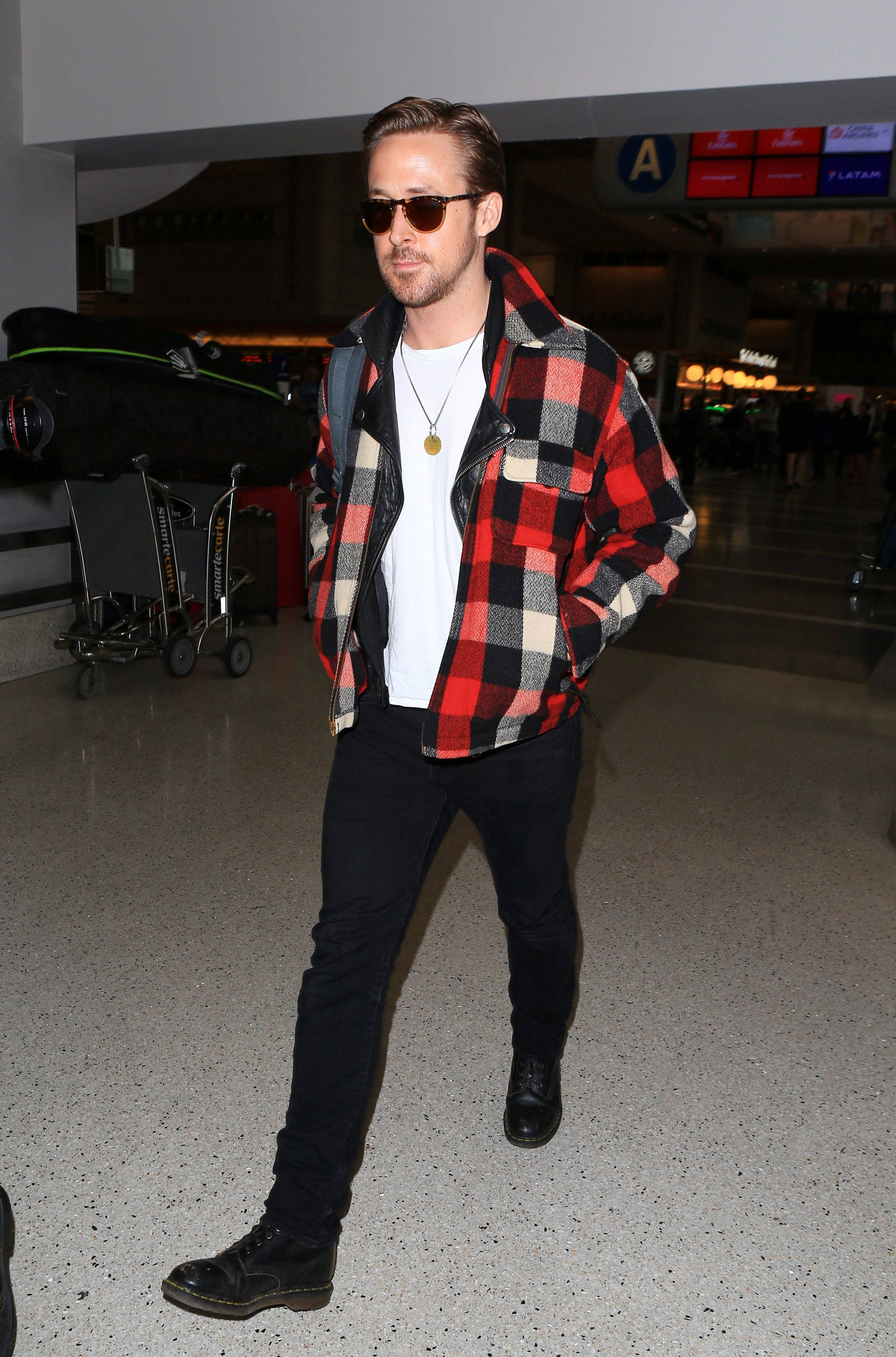 Ryan Gosling 桌布 壁紙 — 萊恩葛斯林穿過機場航廈，身穿紅黑白格紋外套、太陽眼鏡和深色牛仔褲。