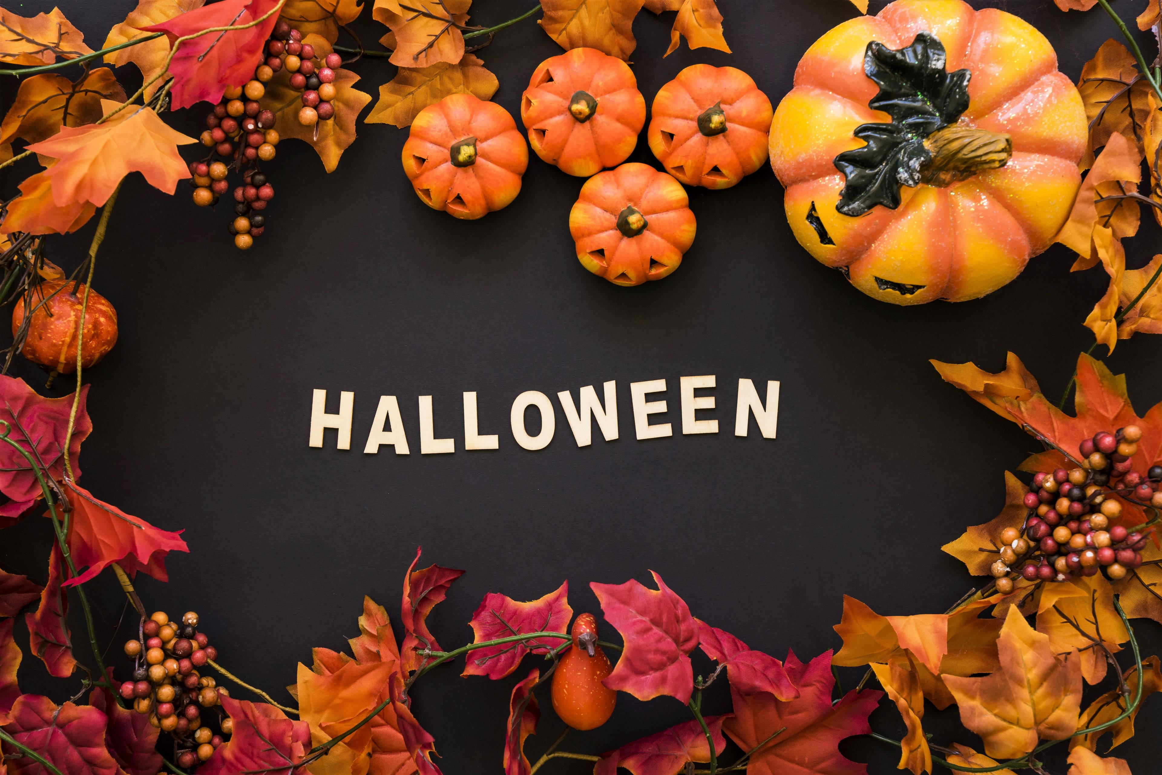 Halloween Aesthetic 桌布 壁紙 — 萬聖節以白色字母拼寫，周圍環繞著橙色南瓜和秋葉，背景為黑色。
