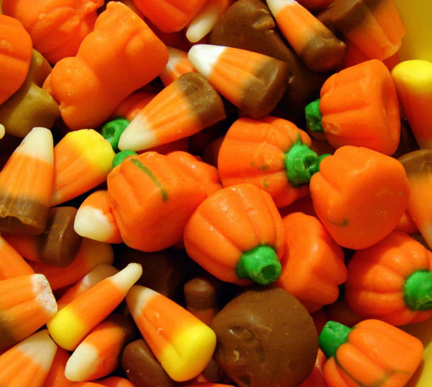 Halloween Treats 桌布 壁紙 — 萬聖節各式糖果的特寫，包括橙色南瓜、綠色莖和糖果玉米，呈現充滿活力的秋季色彩。