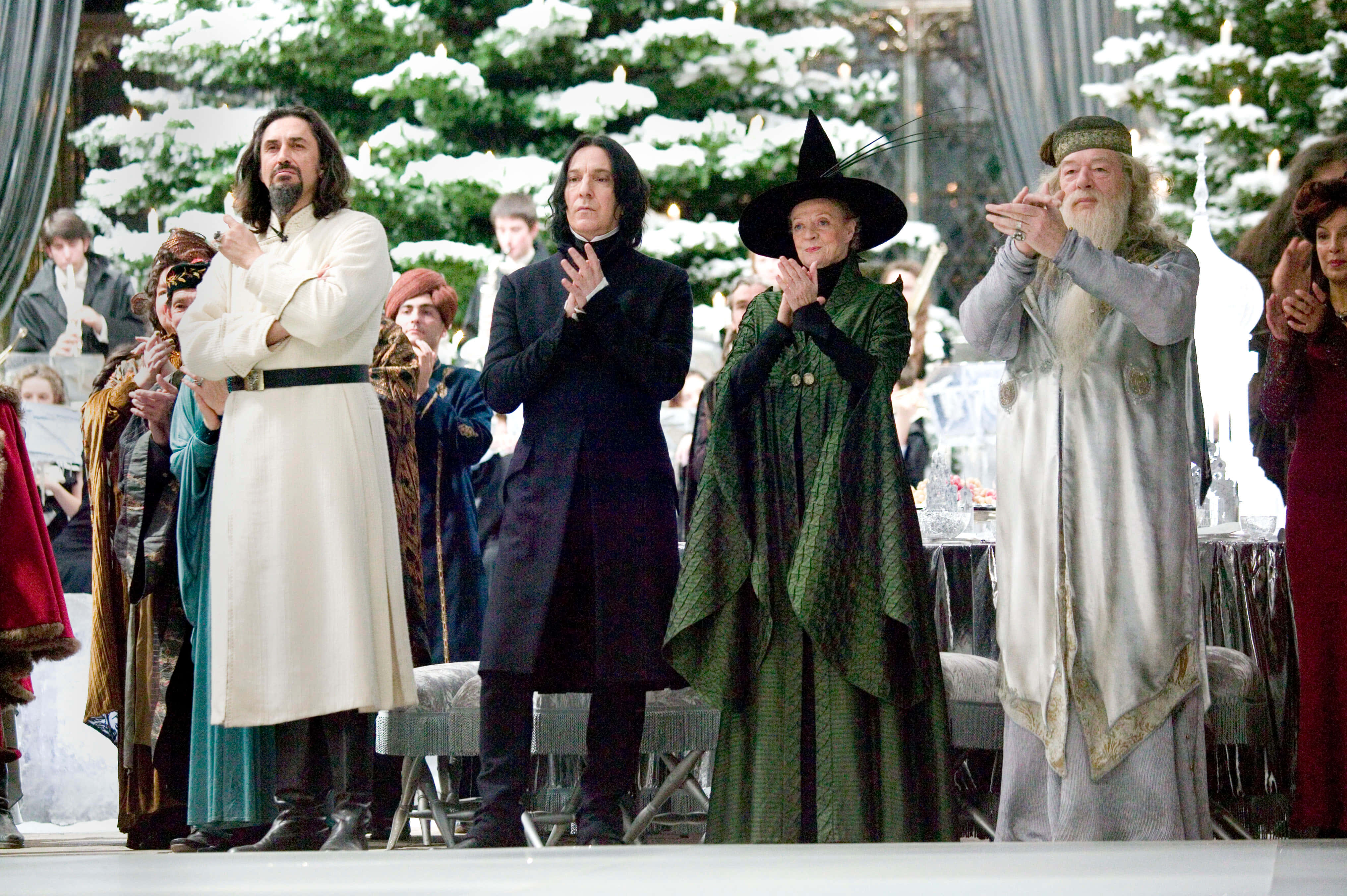 Harry Potter Christmas 桌布 壁紙 — 著名巫師人物身穿華麗長袍，在裝飾樹木下的雪白冬日慶典中鼓掌。