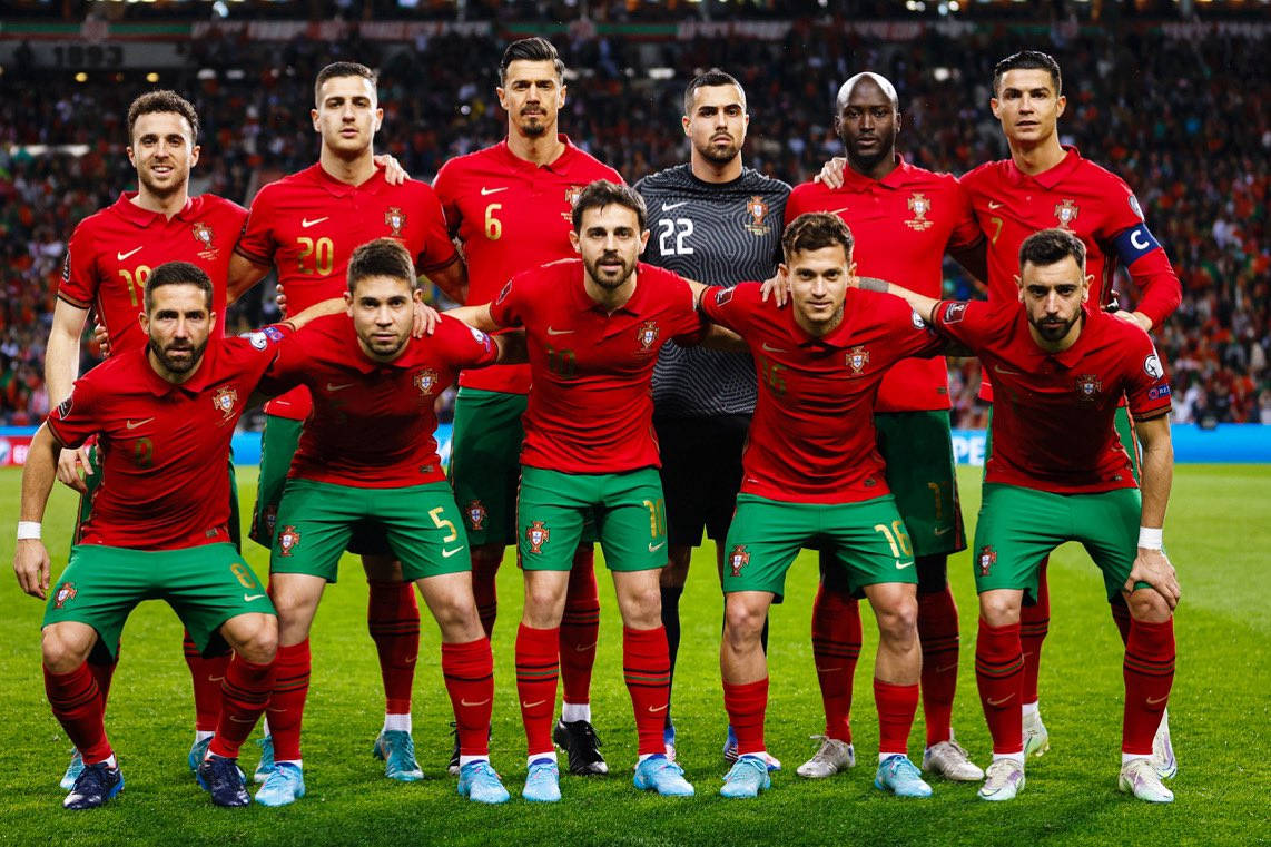 Portugal 桌布 壁紙 — 葡萄牙國家足球隊在明亮的燈光下，於充滿活力的球場草地上，身穿紅色球衣和綠色短褲擺姿勢。