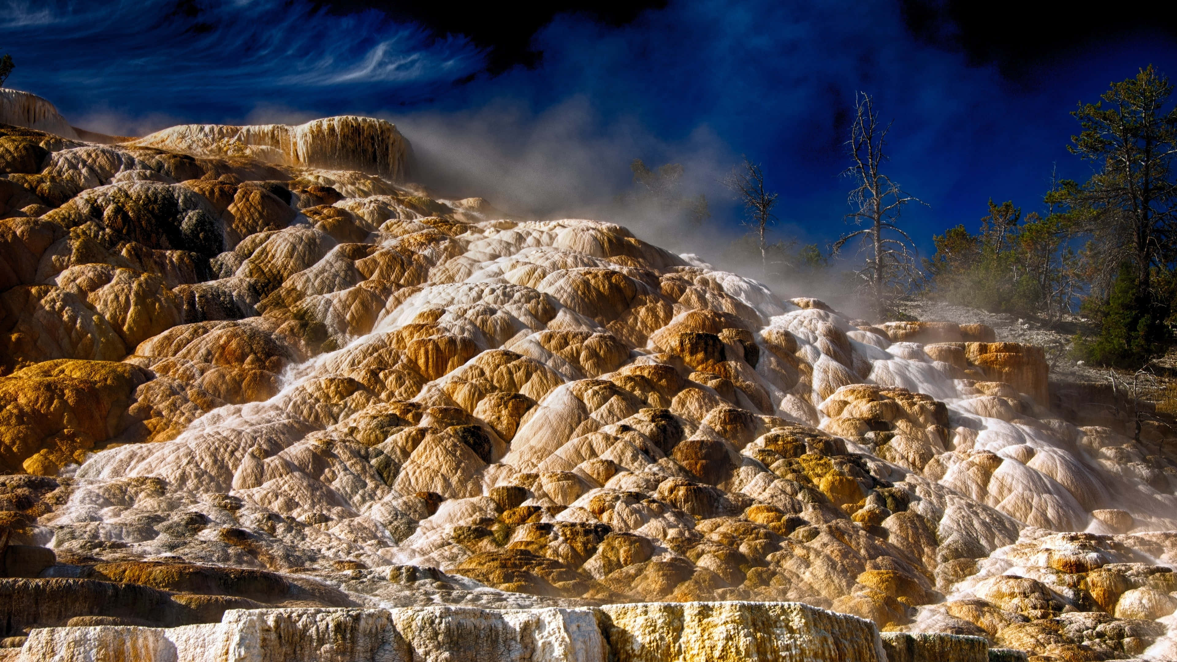 Yellowstone 桌布 壁紙 — 蒸氣從充滿活力的橙色和白色礦物梯田升起，在戲劇性的深藍色天空下。