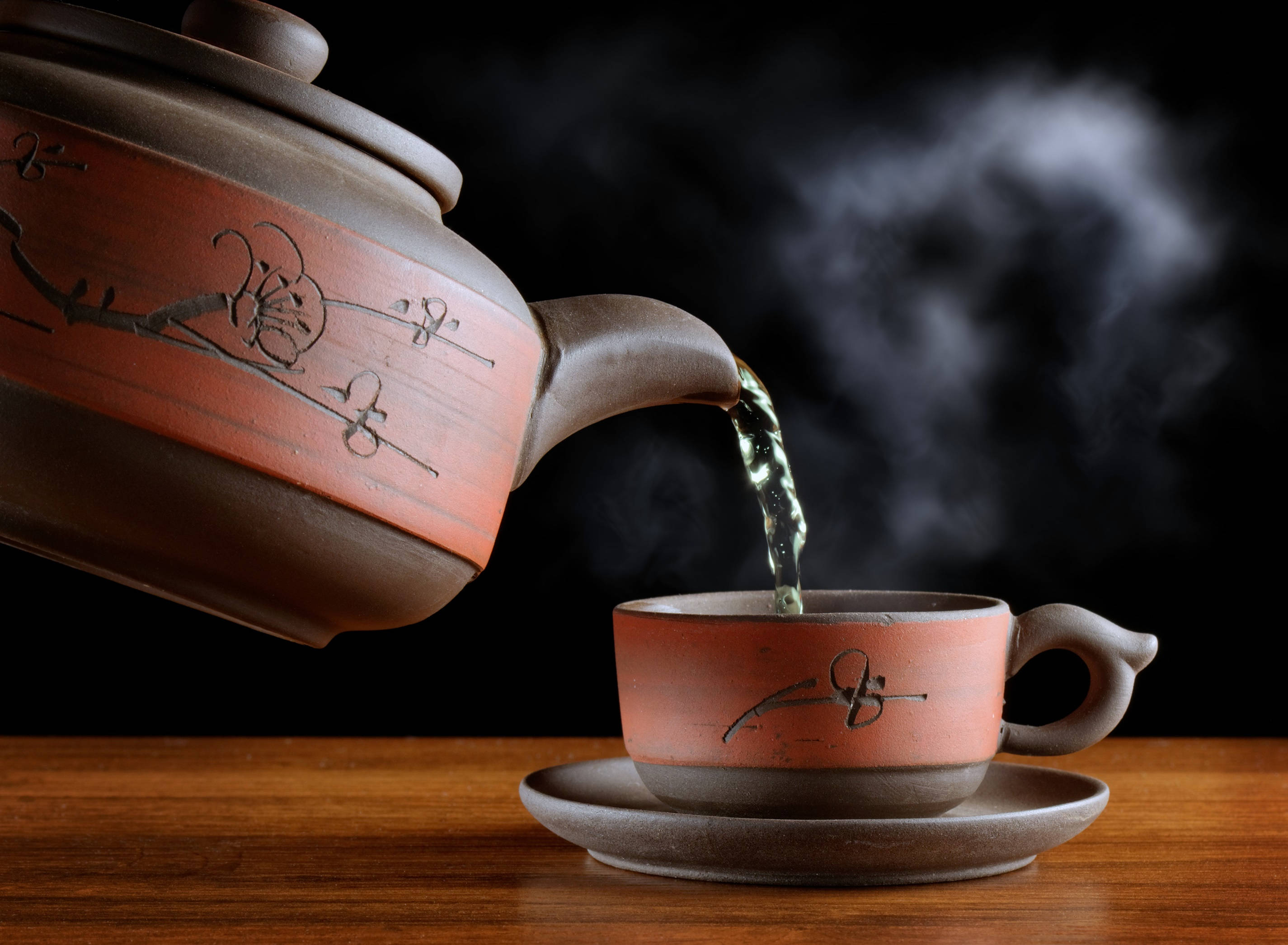 tea 桌布 壁紙 — 蒸氣騰騰的綠茶從陶瓷茶壺倒入相配的茶杯中，放在木桌上，背景為深色。