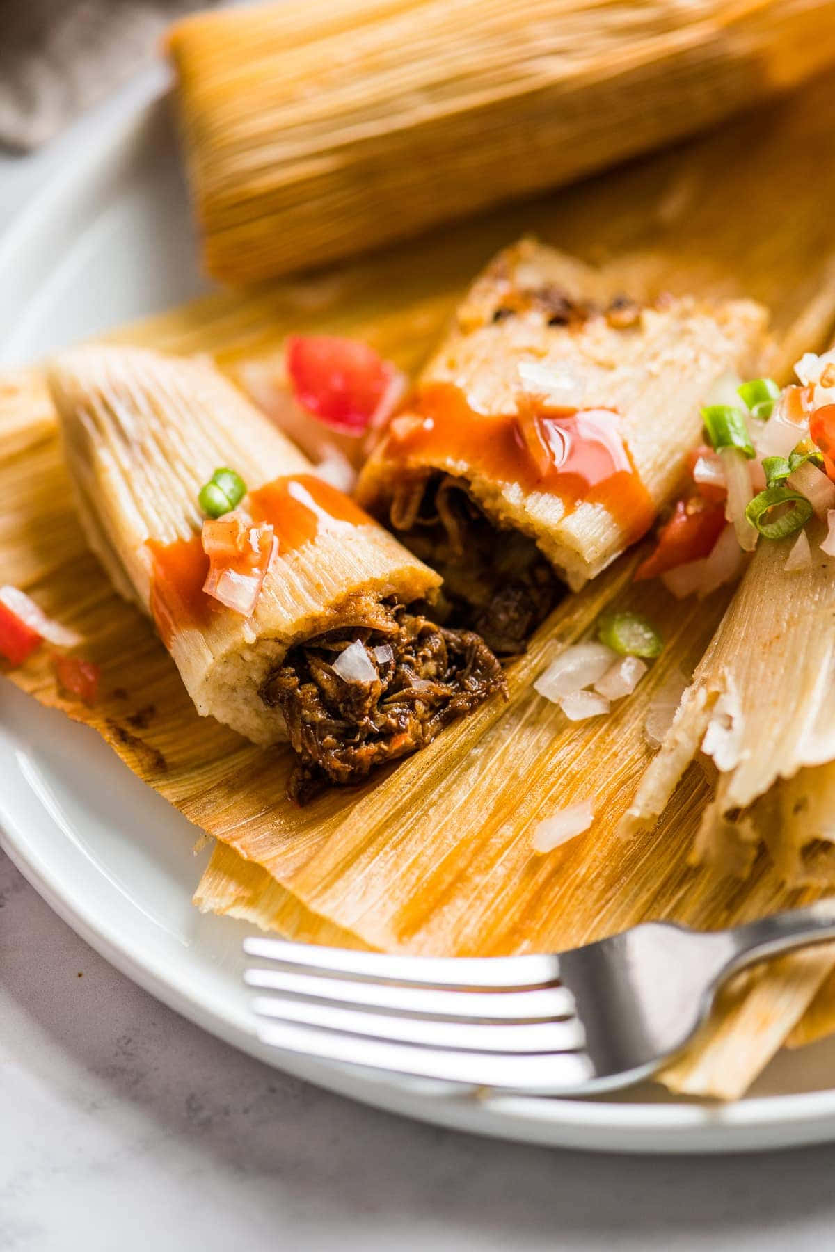 Mexican 桌布 壁紙 — 蒸玉米粉糰切開的特寫，露出美味的肉餡，上面澆有紅醬、切碎的洋蔥和青辣椒，放在白色盤子上。